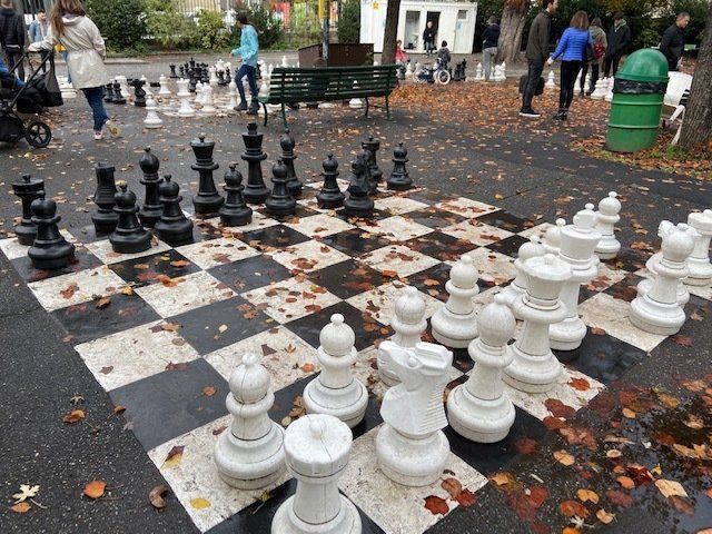A large chess board is sitting on the ground in a park.