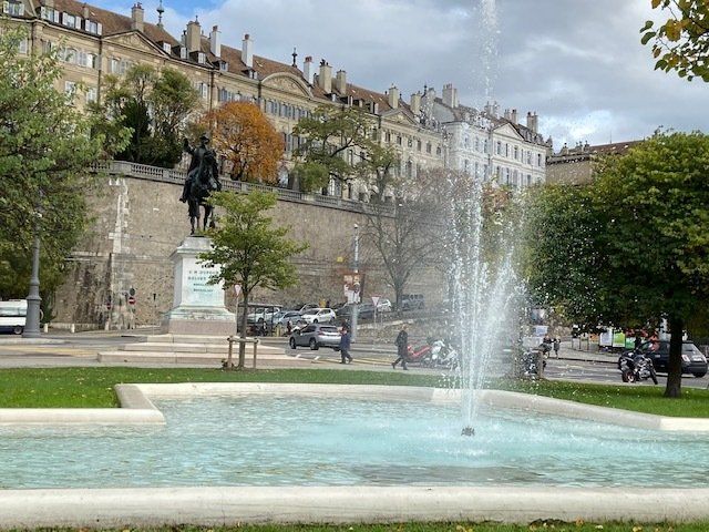A fountain in a park with a statue in the background