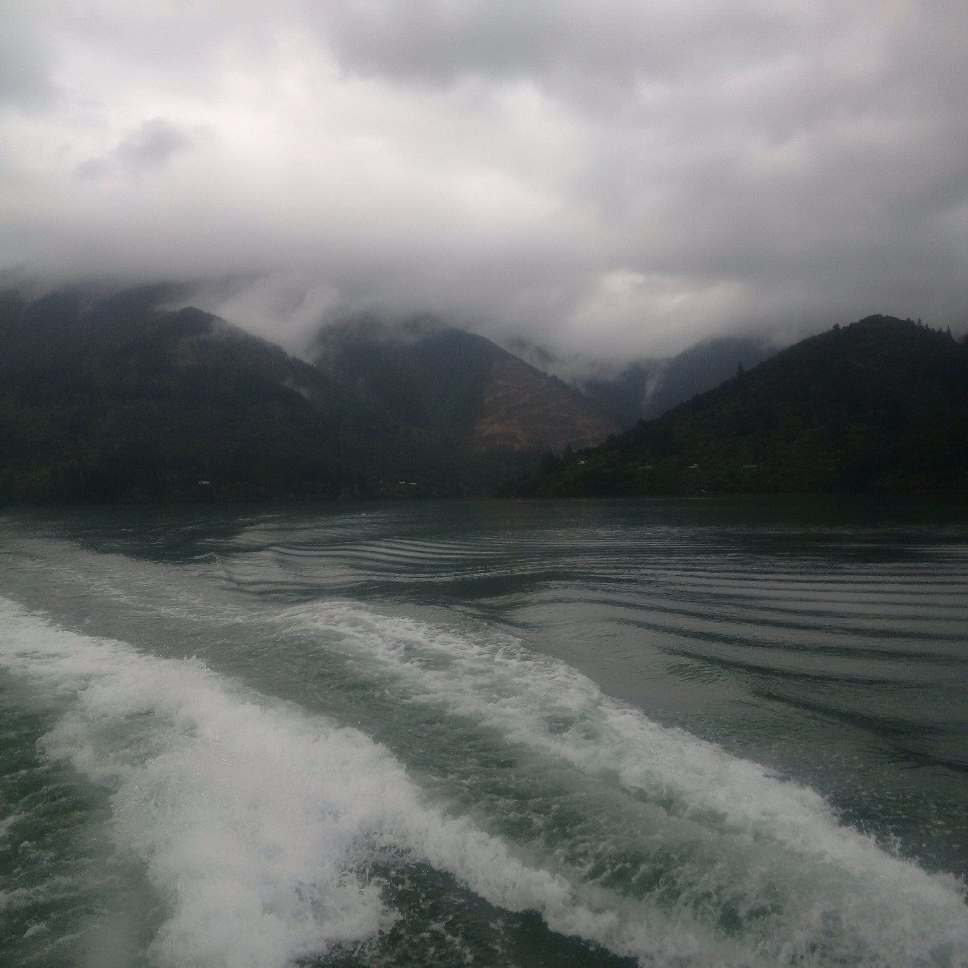 A boat is floating on a lake with mountains in the background on a cloudy day.