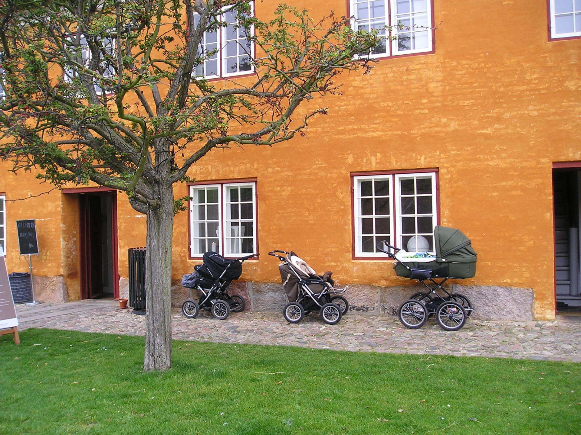 Three stroller are parked in front of an orange building
