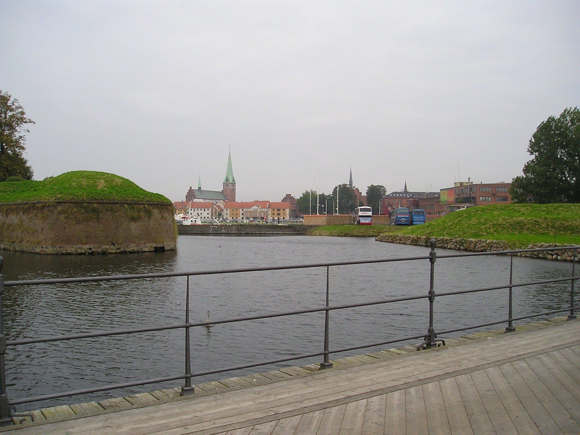 A fence surrounds a body of water with a city in the background