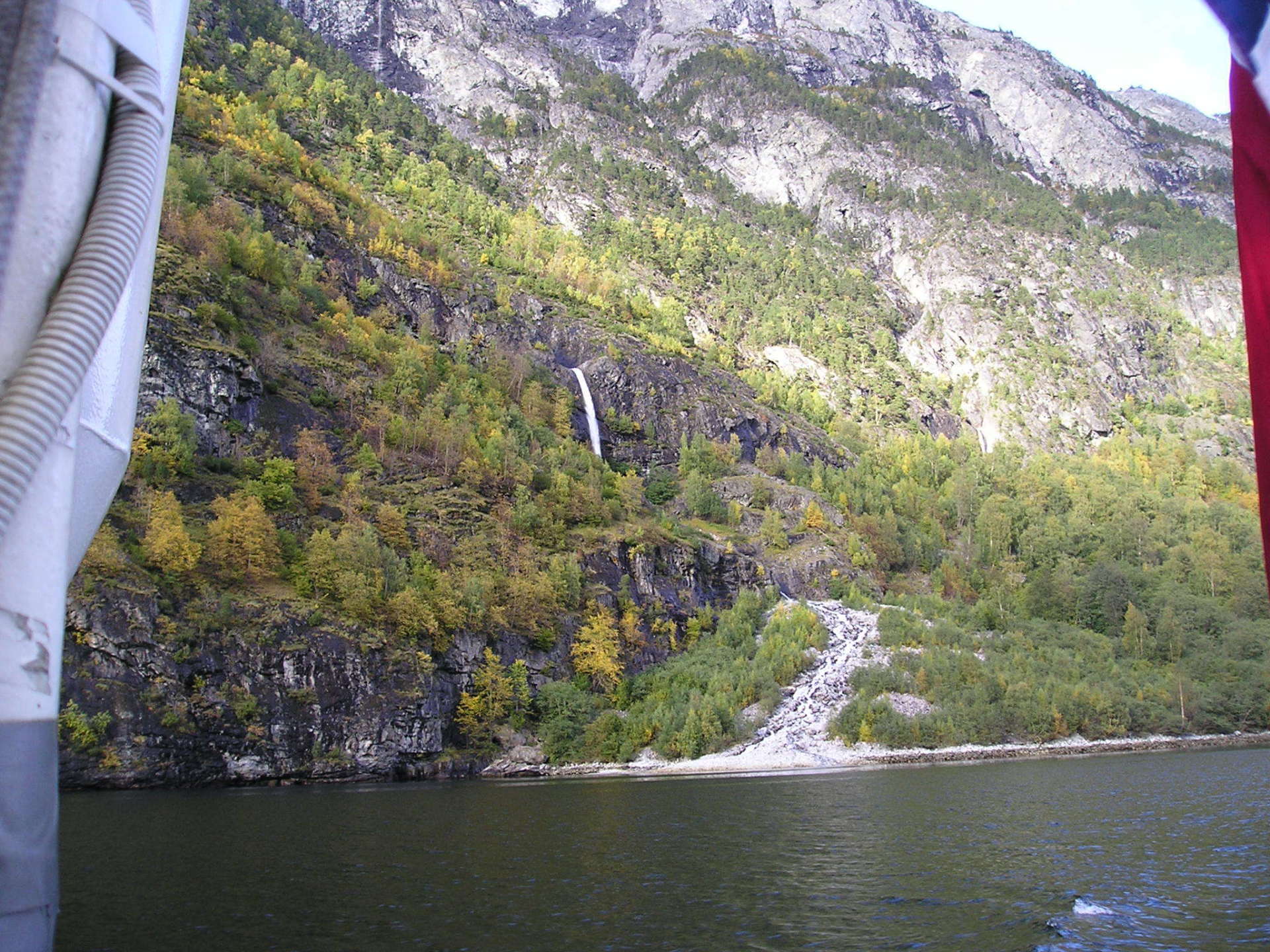 A waterfall is on the side of a mountain next to a body of water.