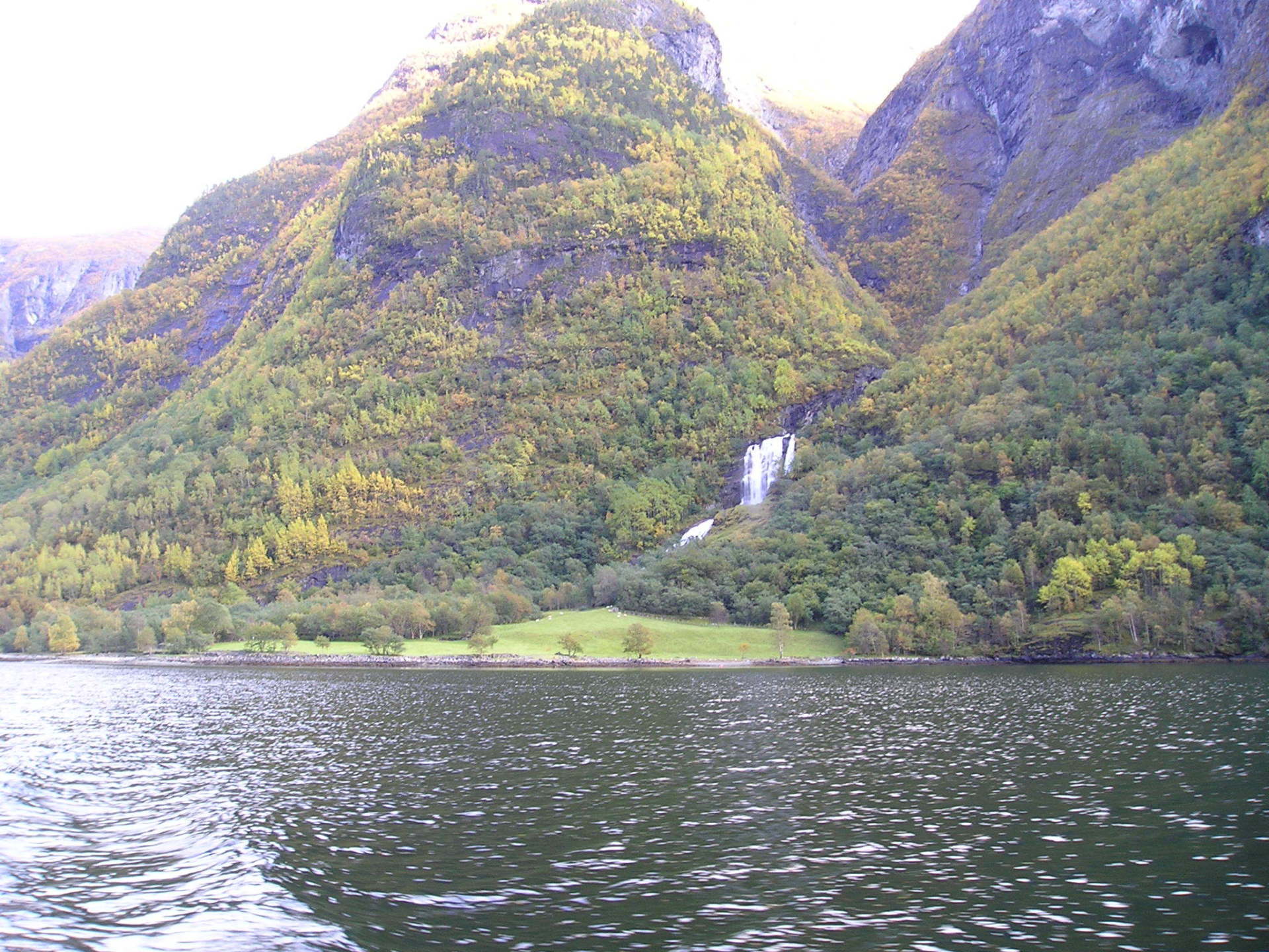 A waterfall is surrounded by mountains and trees near a lake