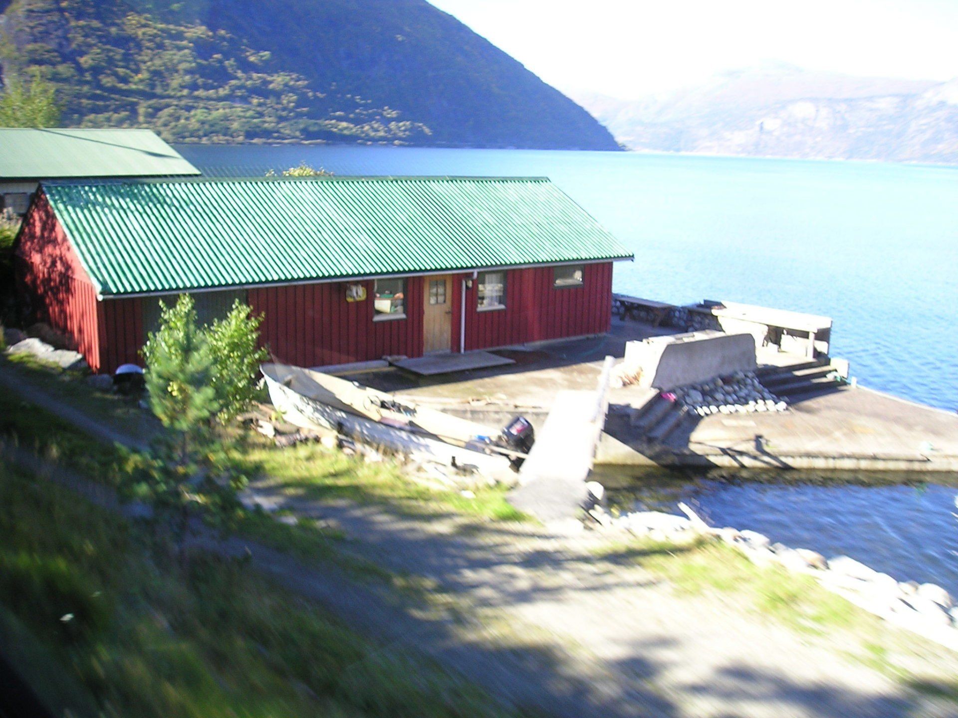 A red building with a green roof sits next to a body of water