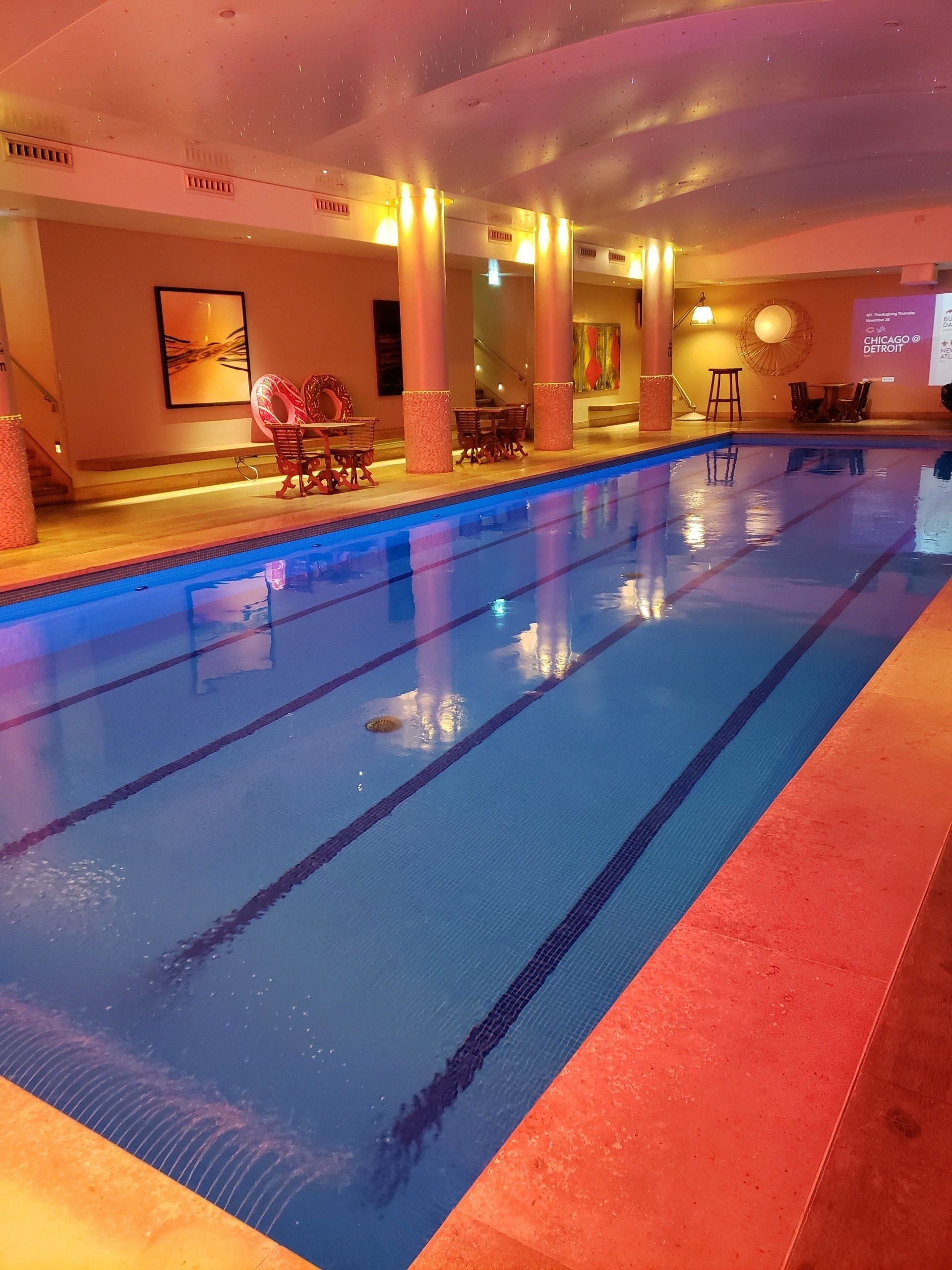 A large indoor swimming pool with a table and chairs in the background.