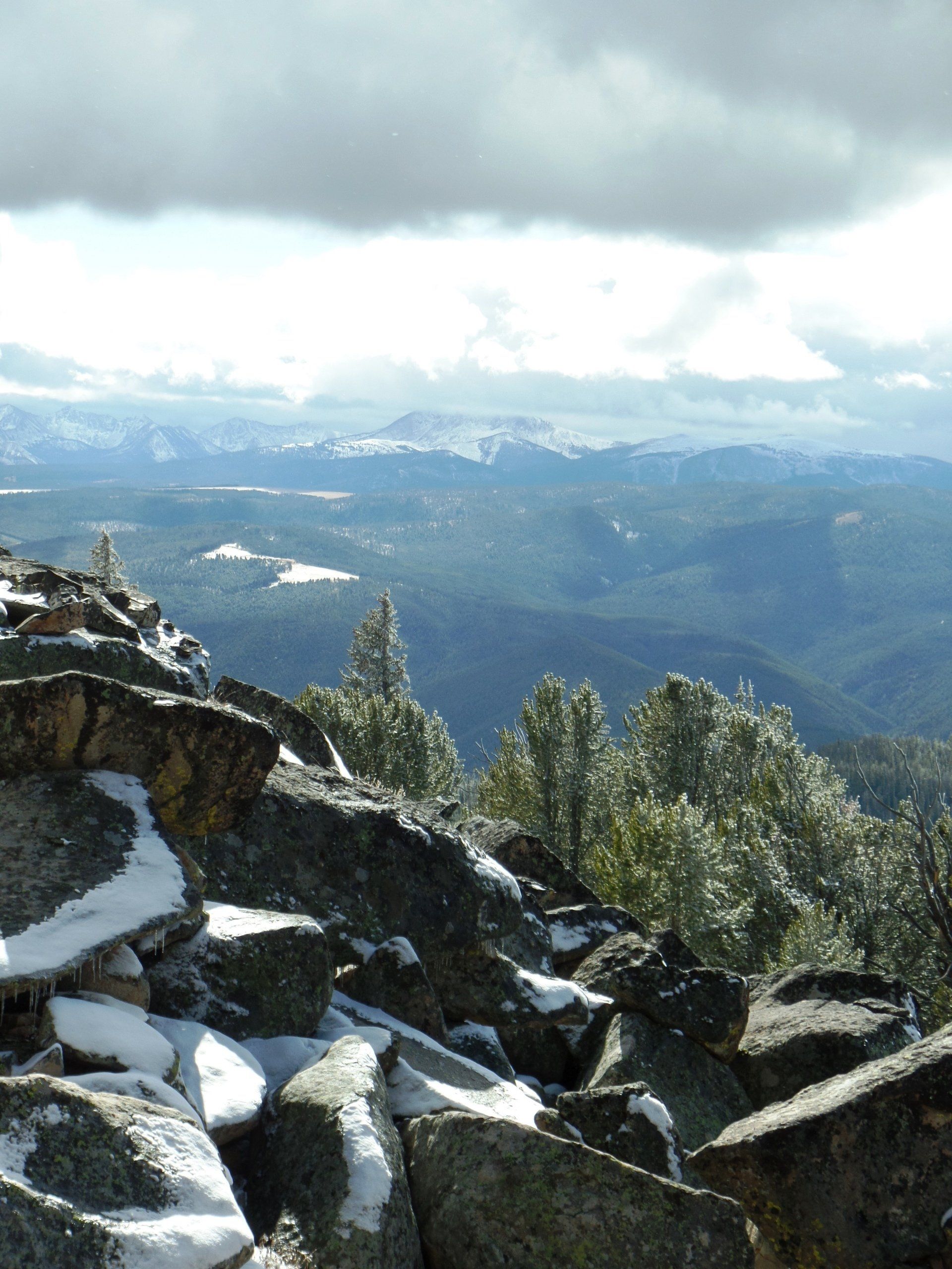 A rocky hillside with snow on it and mountains in the background