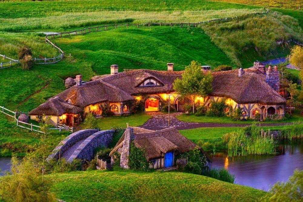 A large house with a thatched roof is in the middle of a lush green field.