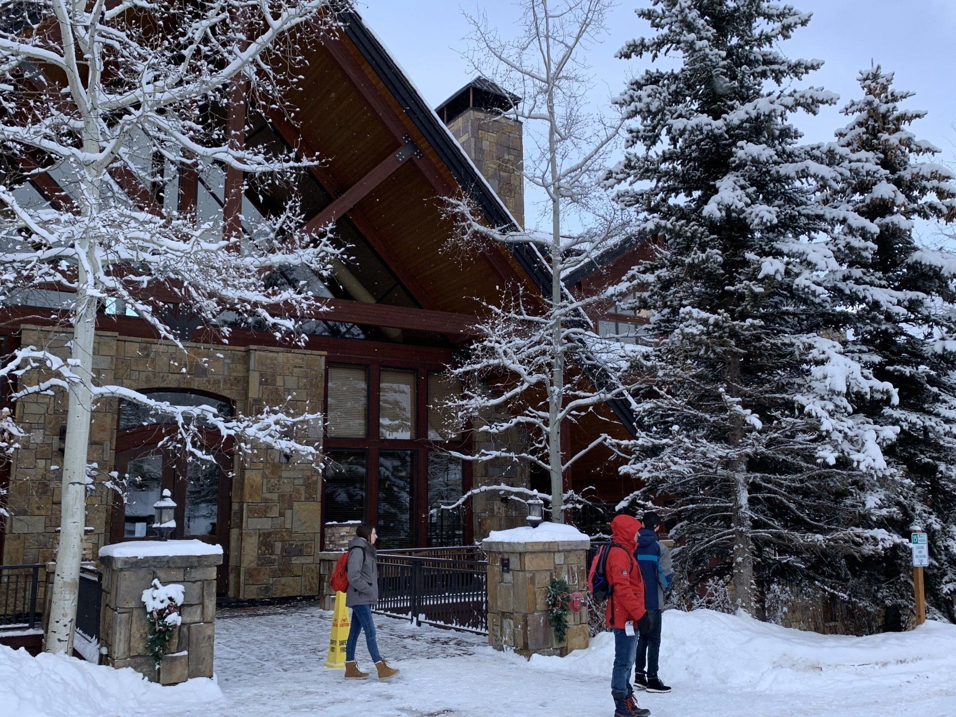 A group of people are walking in the snow in front of a house.