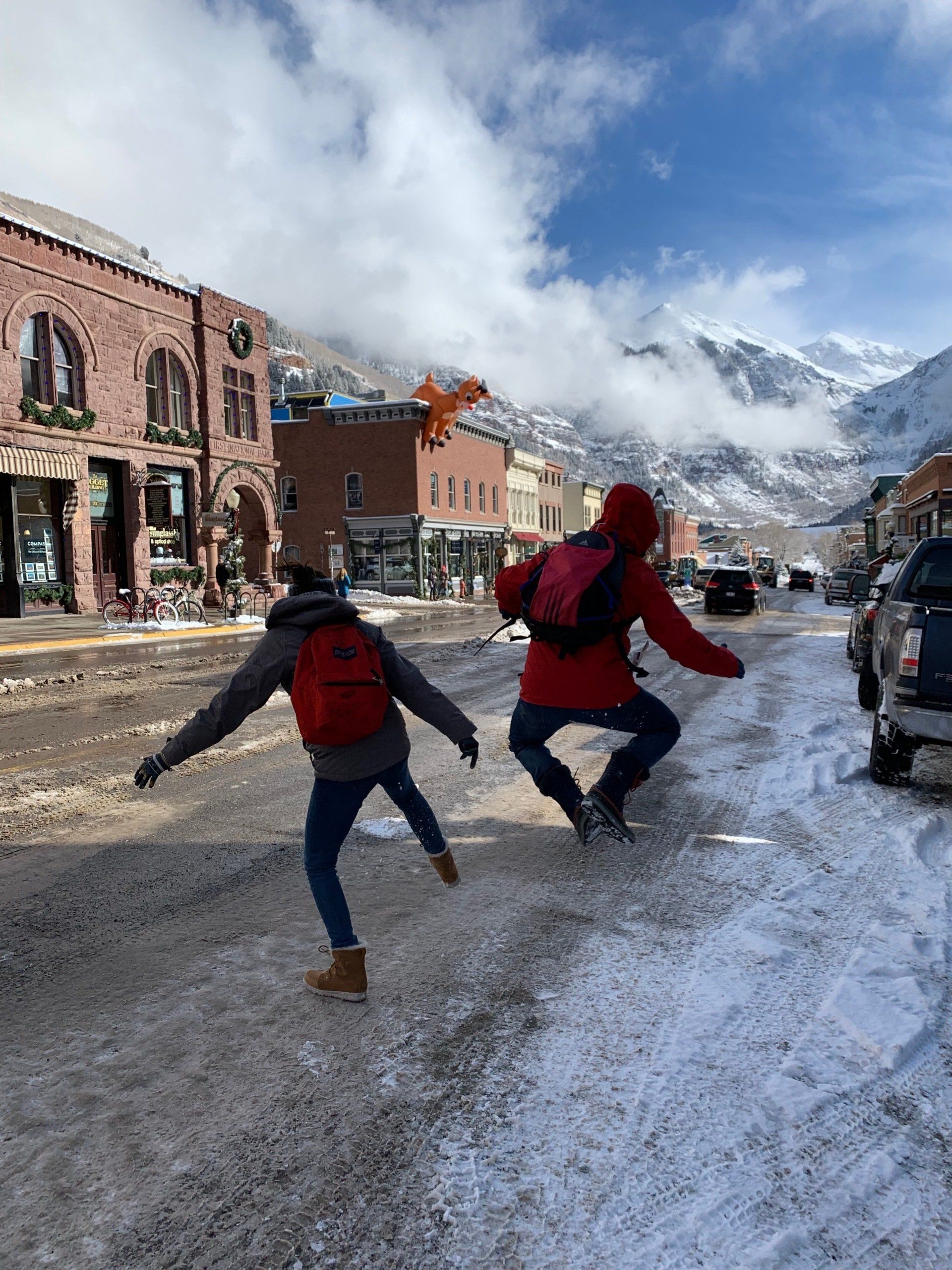 Two people are playing in the snow on a city street.