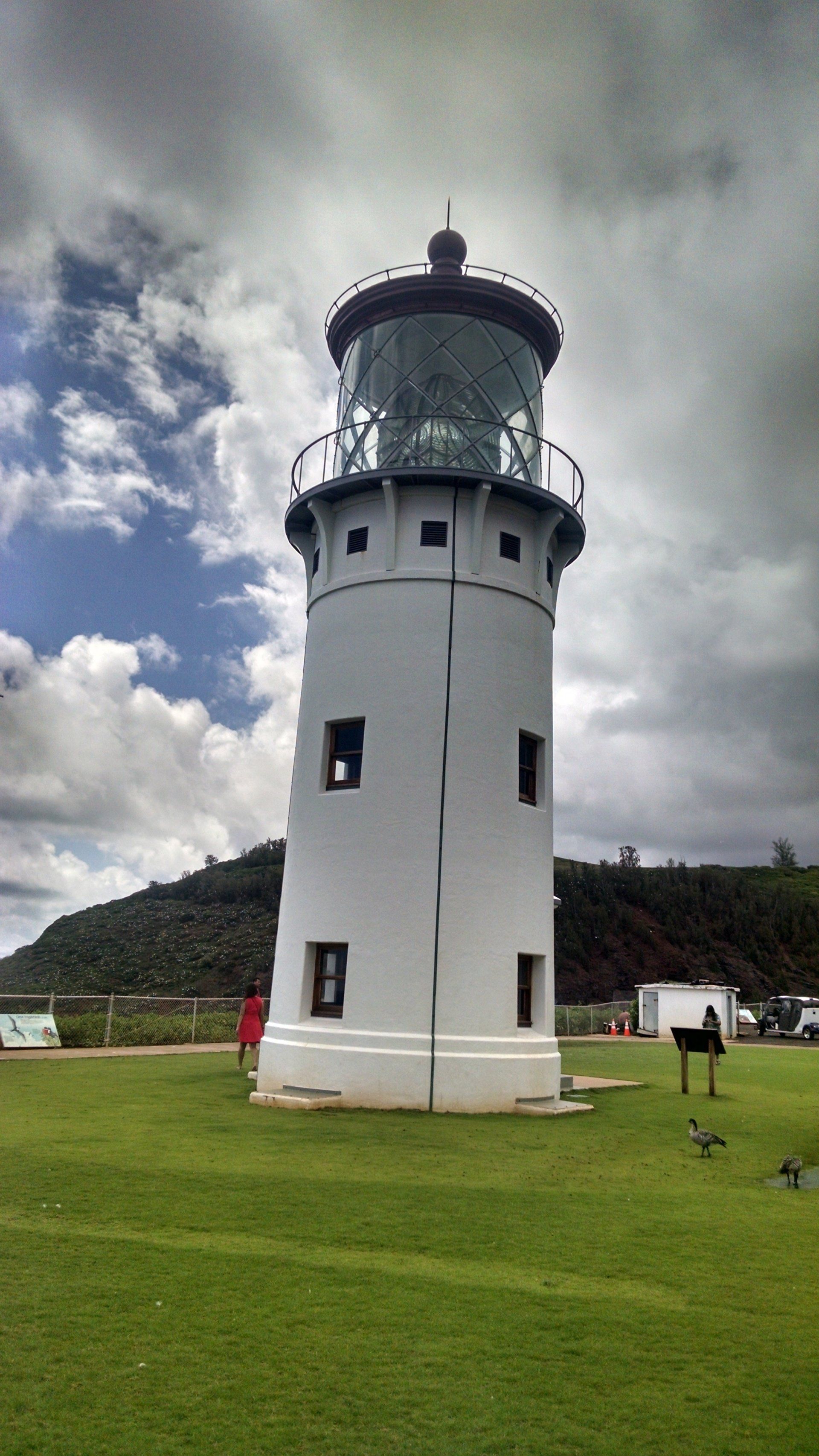 A white lighthouse is sitting on top of a lush green field.