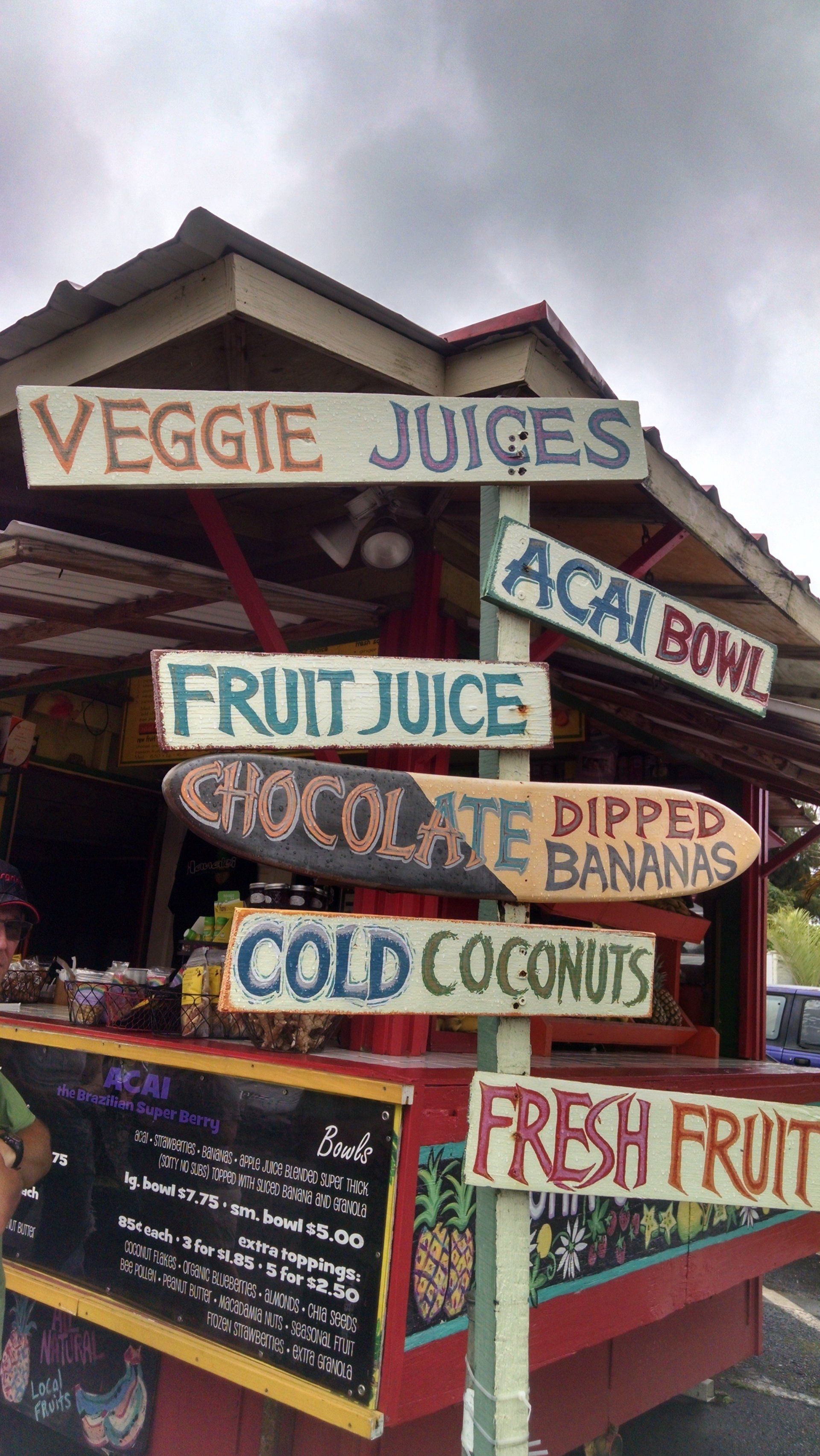 A sign for veggie juices acai bowl fruit juice chocolate dipped bananas cold coconuts and fresh fruit