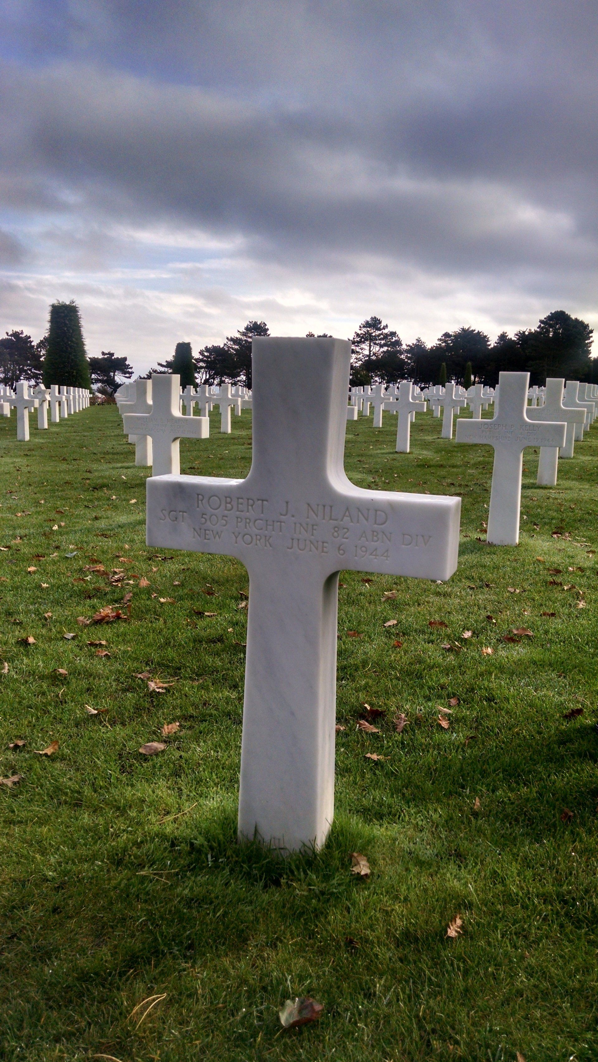 A white cross is in the middle of a cemetery.