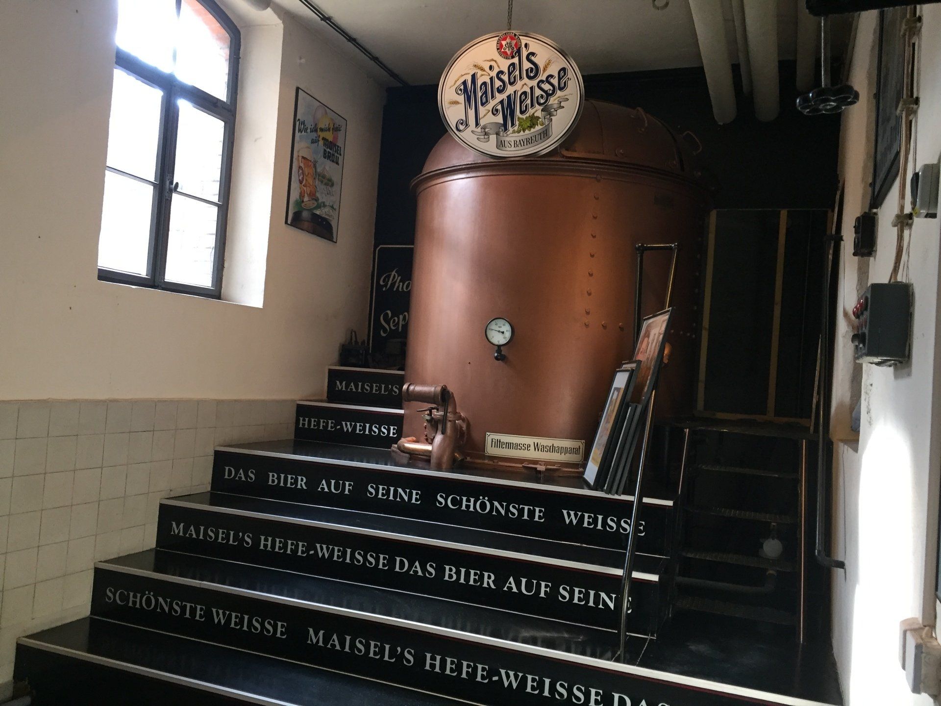 A room with stairs leading up to a large copper tank.