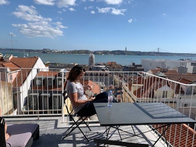 A woman is sitting at a table on a balcony overlooking a body of water.