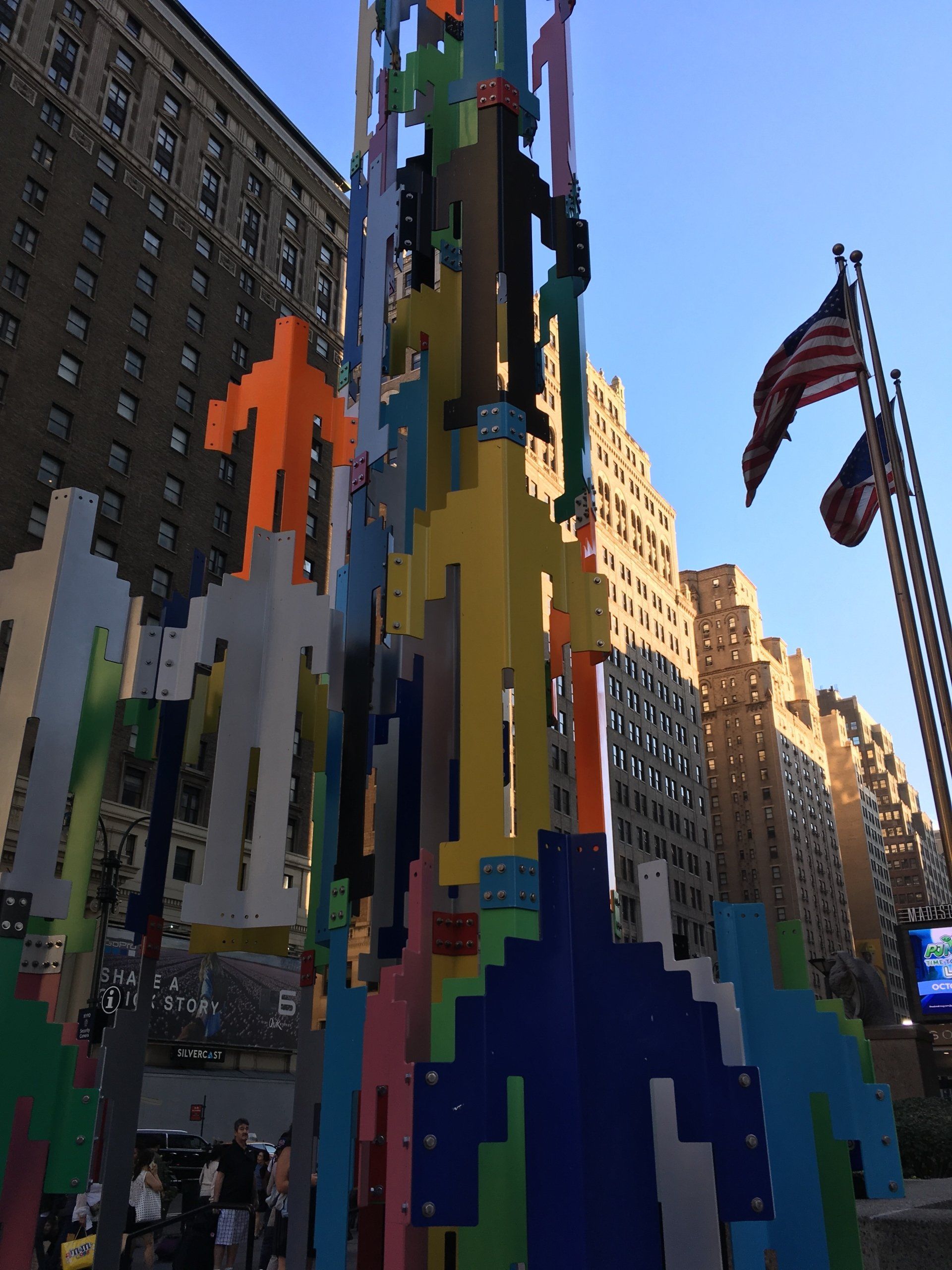 A colorful sculpture in front of a building with flags in the background