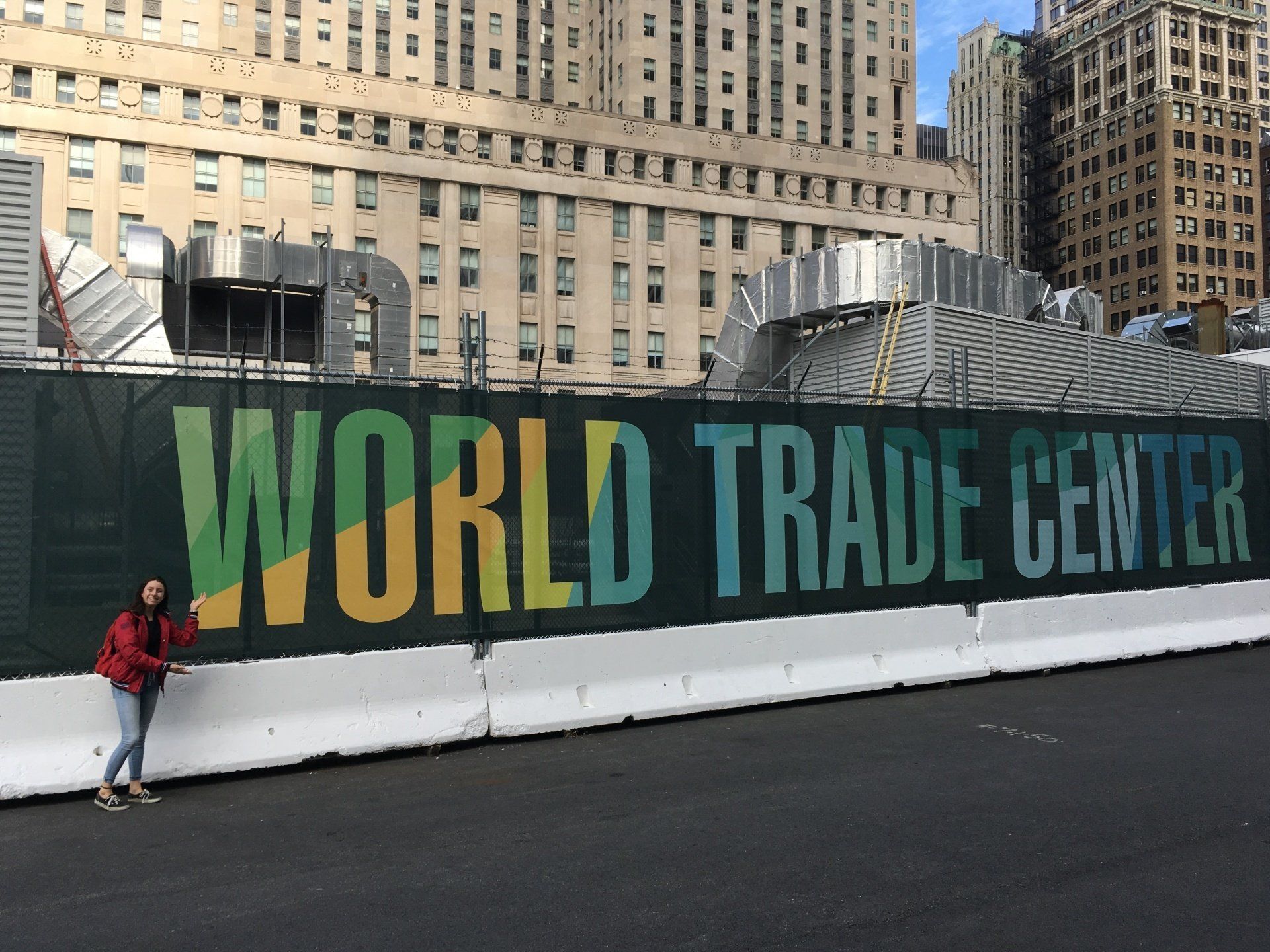 A woman stands in front of a fence that says world trade center