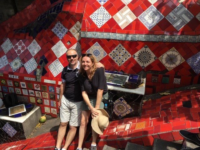 A man and a woman are posing for a picture in front of a wall of tiles