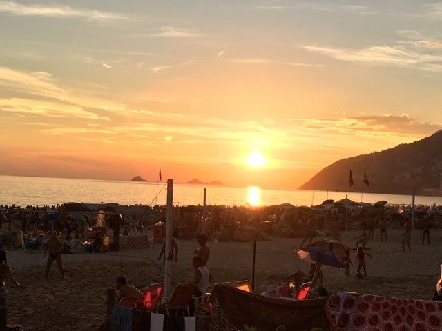 The sun is setting over the ocean and people are gathered on the beach