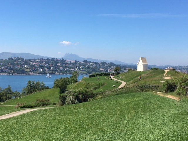 A small white house is sitting on top of a grassy hill overlooking a body of water.