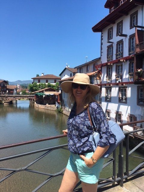 A woman wearing a hat is standing on a bridge over a river
