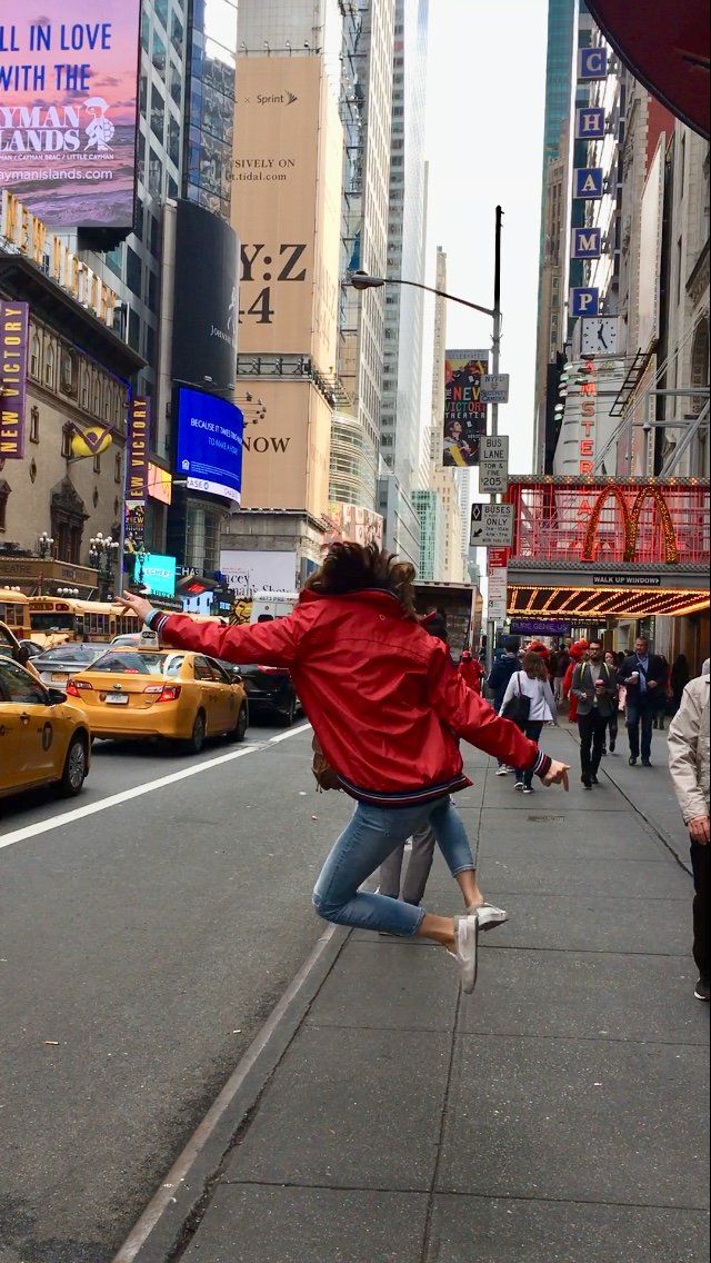 A woman in a red jacket is jumping in the air on a city street