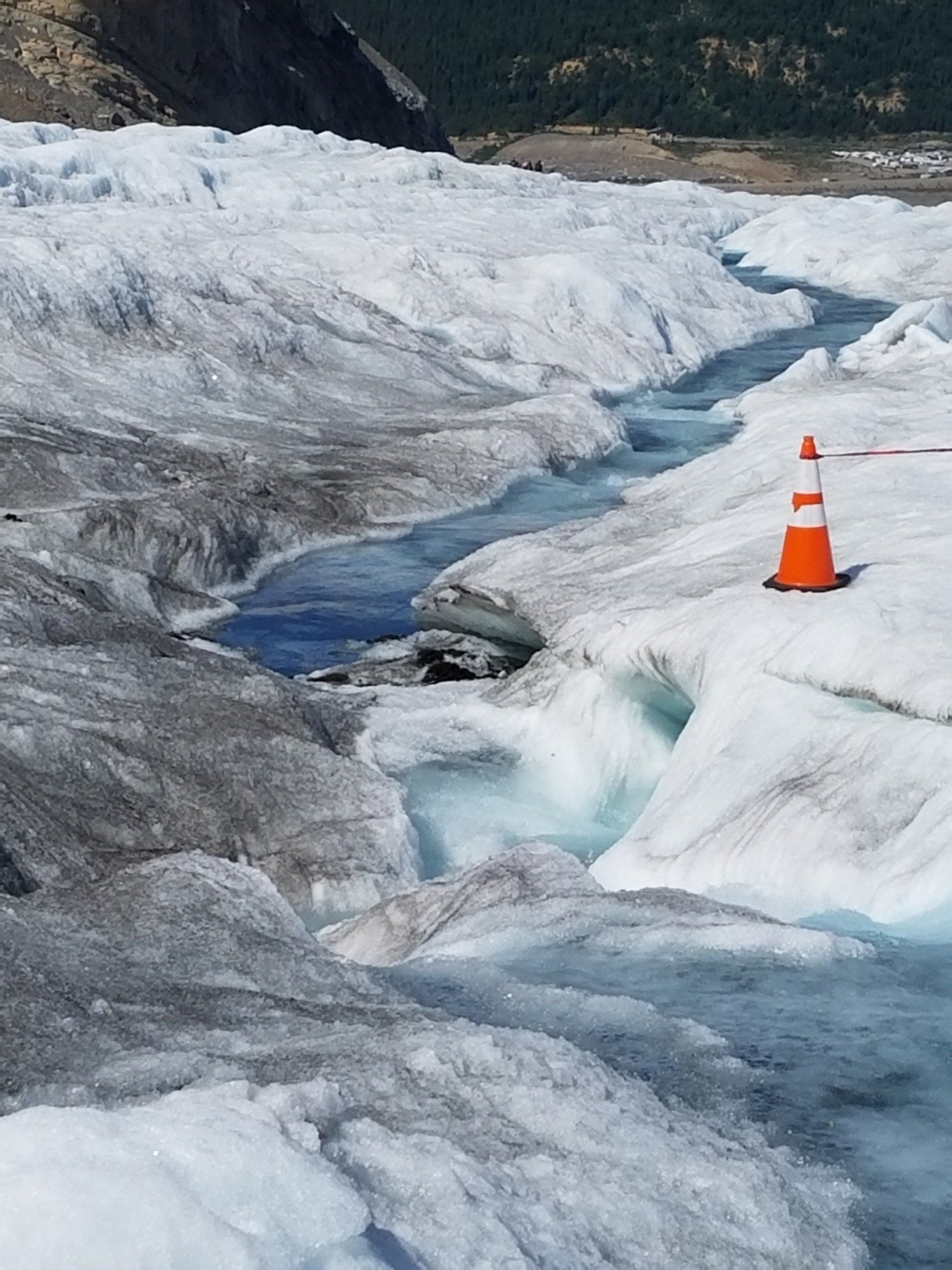 An orange and white traffic cone sits on the side of a frozen river