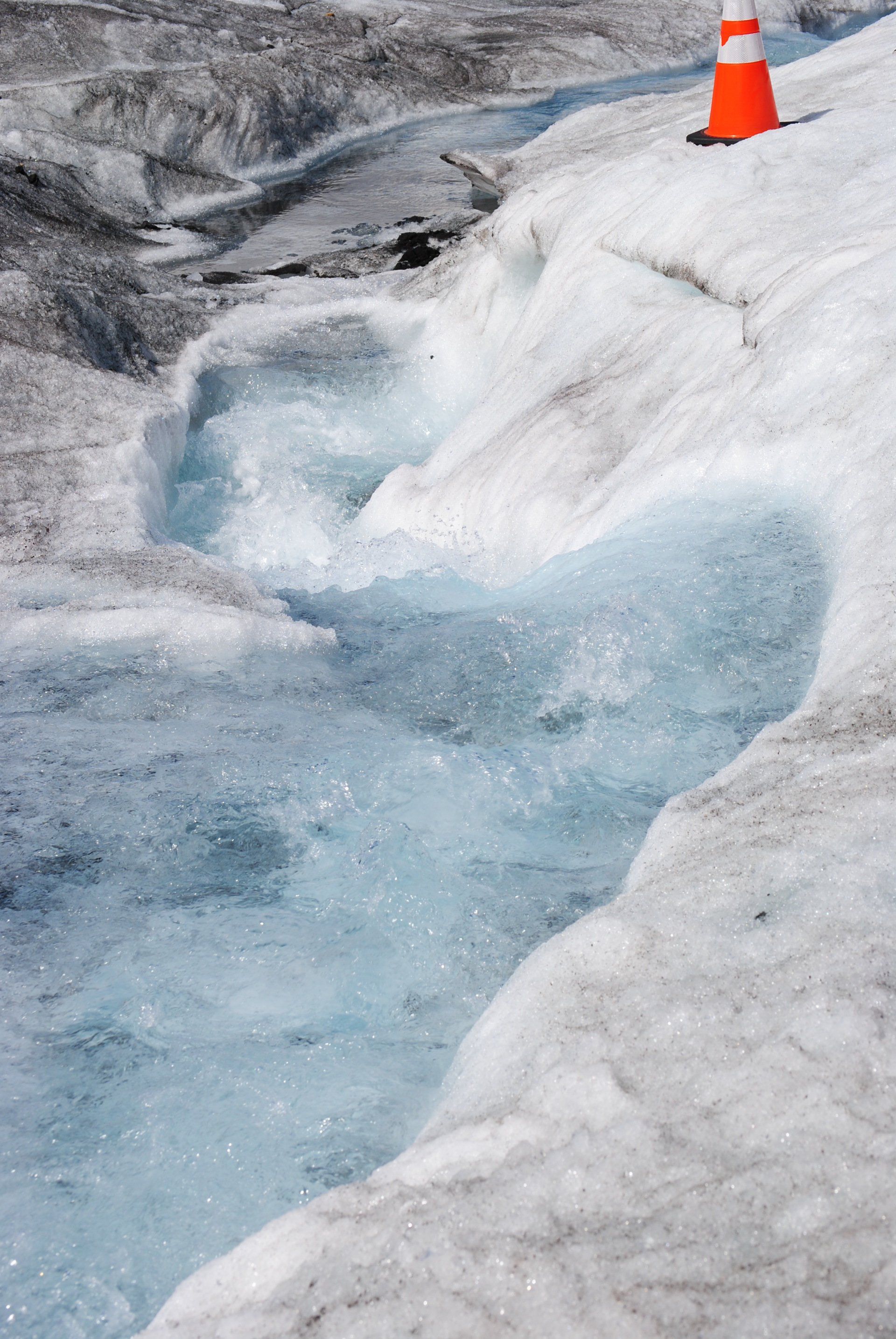 There is a traffic cone on the side of a snowy hill.