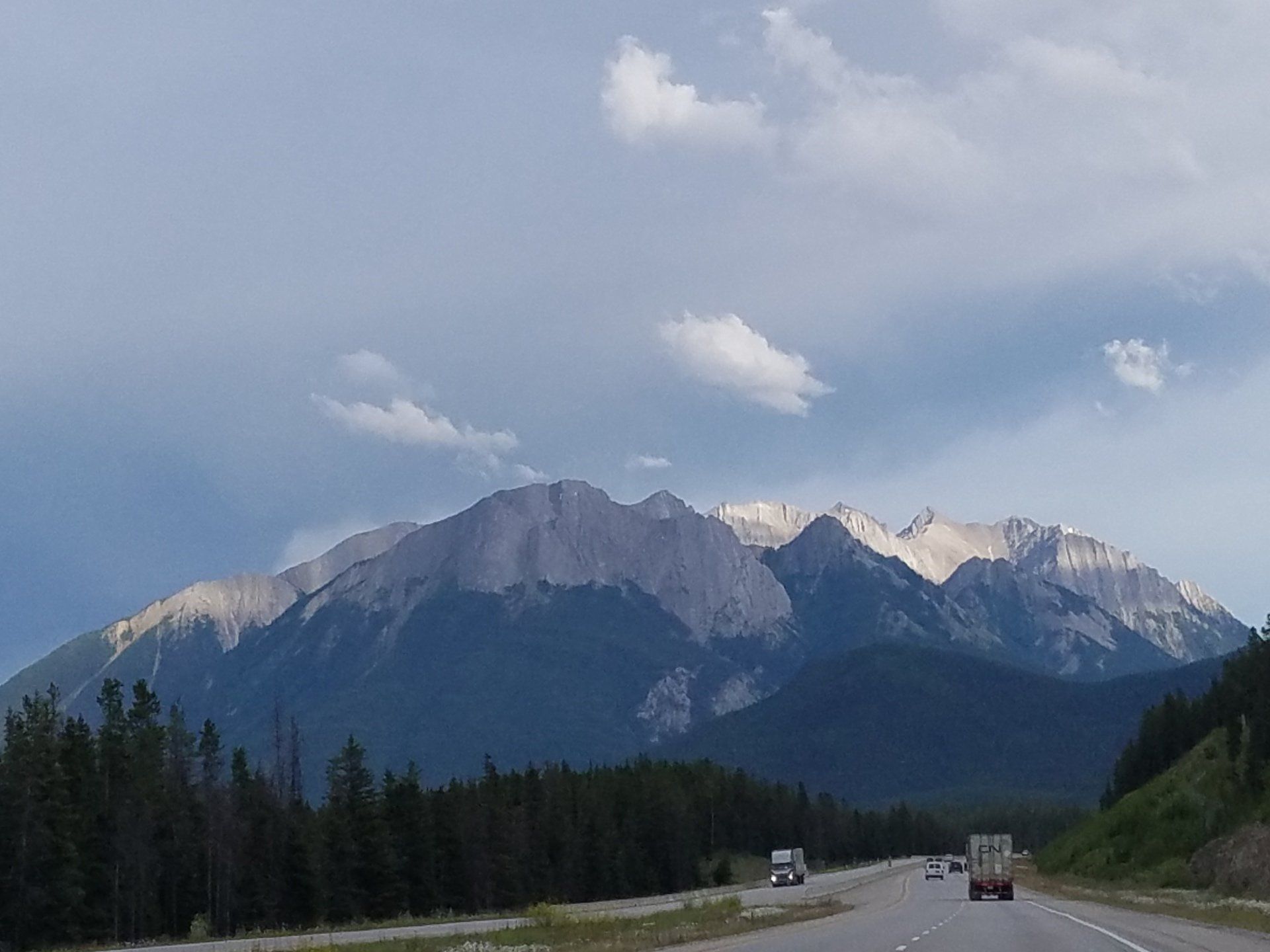 A highway with mountains in the background and trees on the side