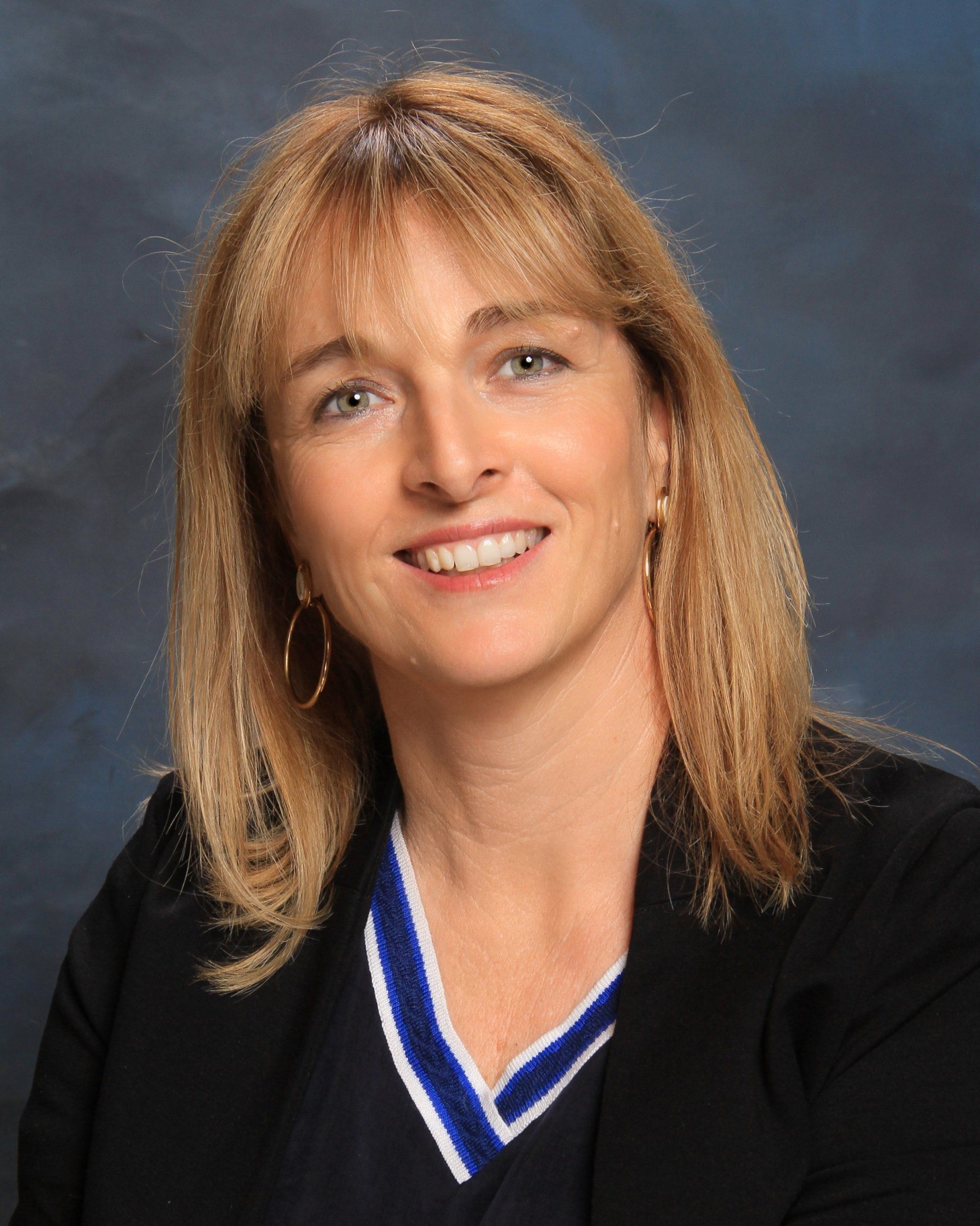 A woman wearing a black jacket and a blue and white sweater smiles for the camera