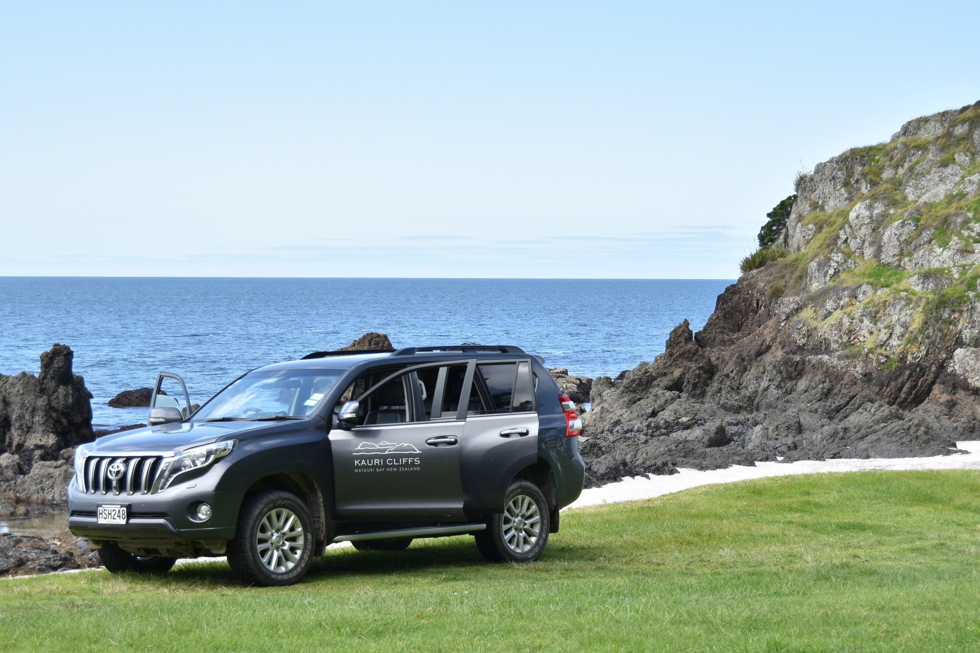 A black suv is parked on the grass near the ocean.