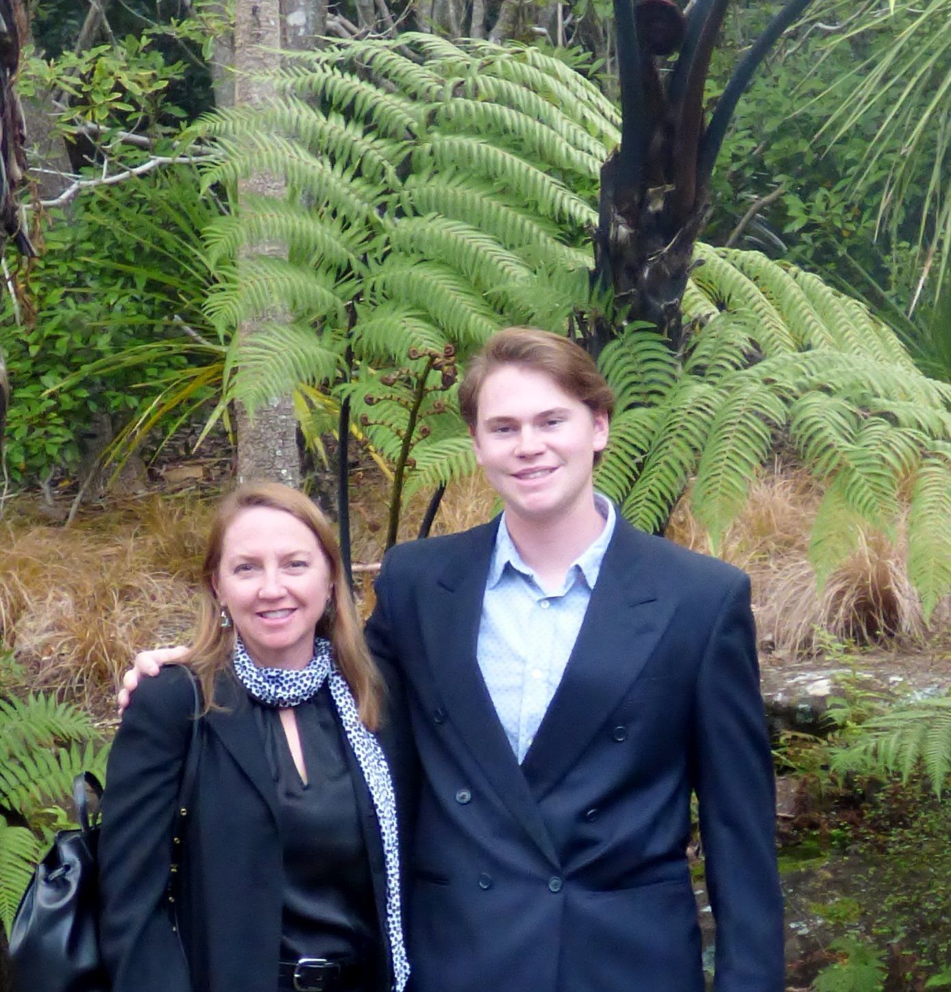A man and a woman pose for a picture in front of ferns