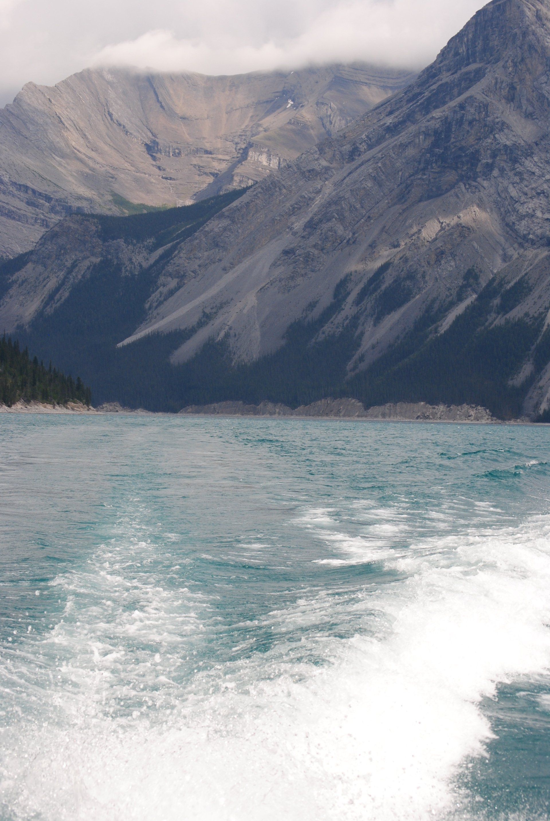 A boat is going through a lake with mountains in the background