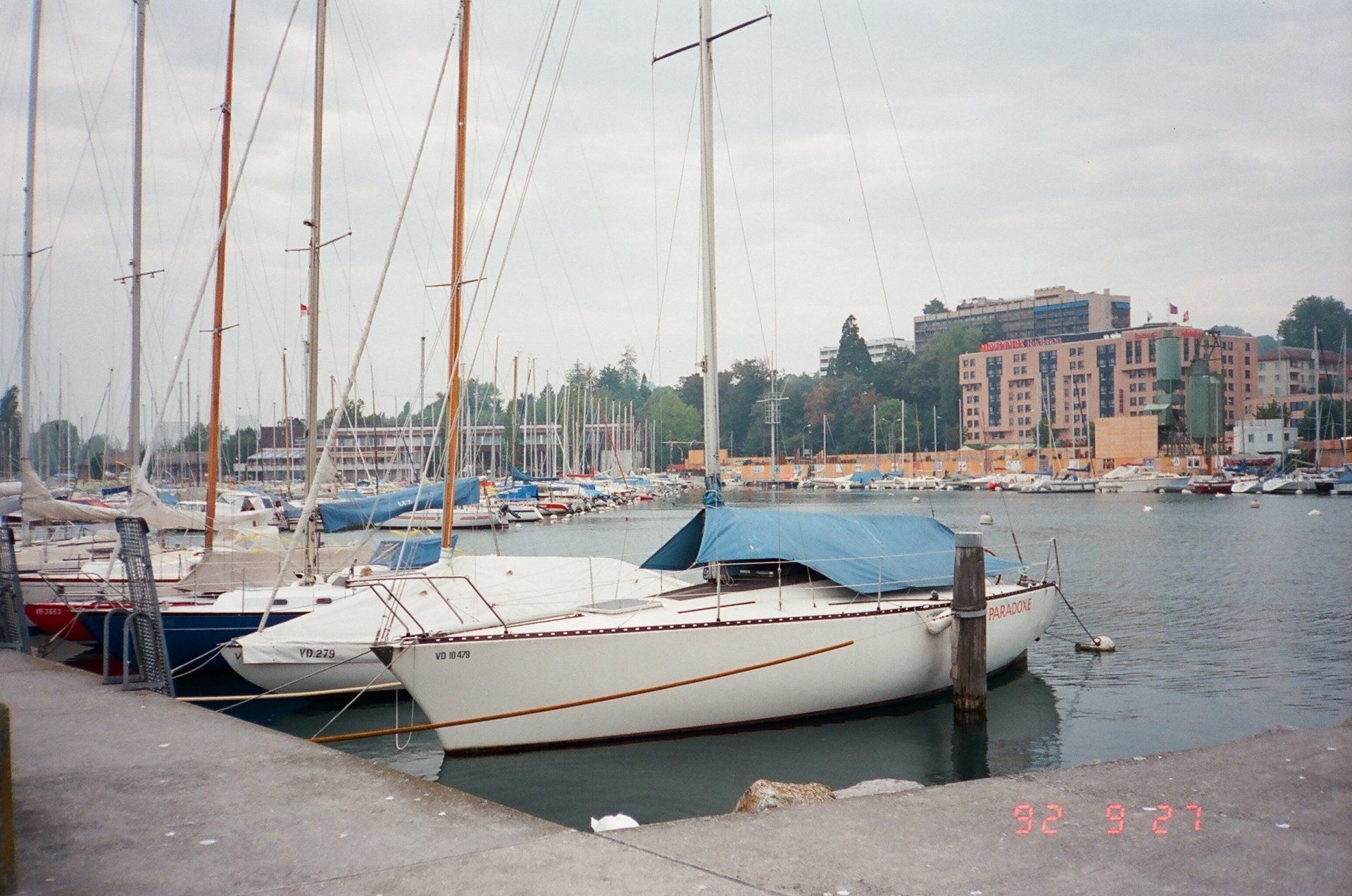 A row of sailboats are docked in a harbor on a cloudy day