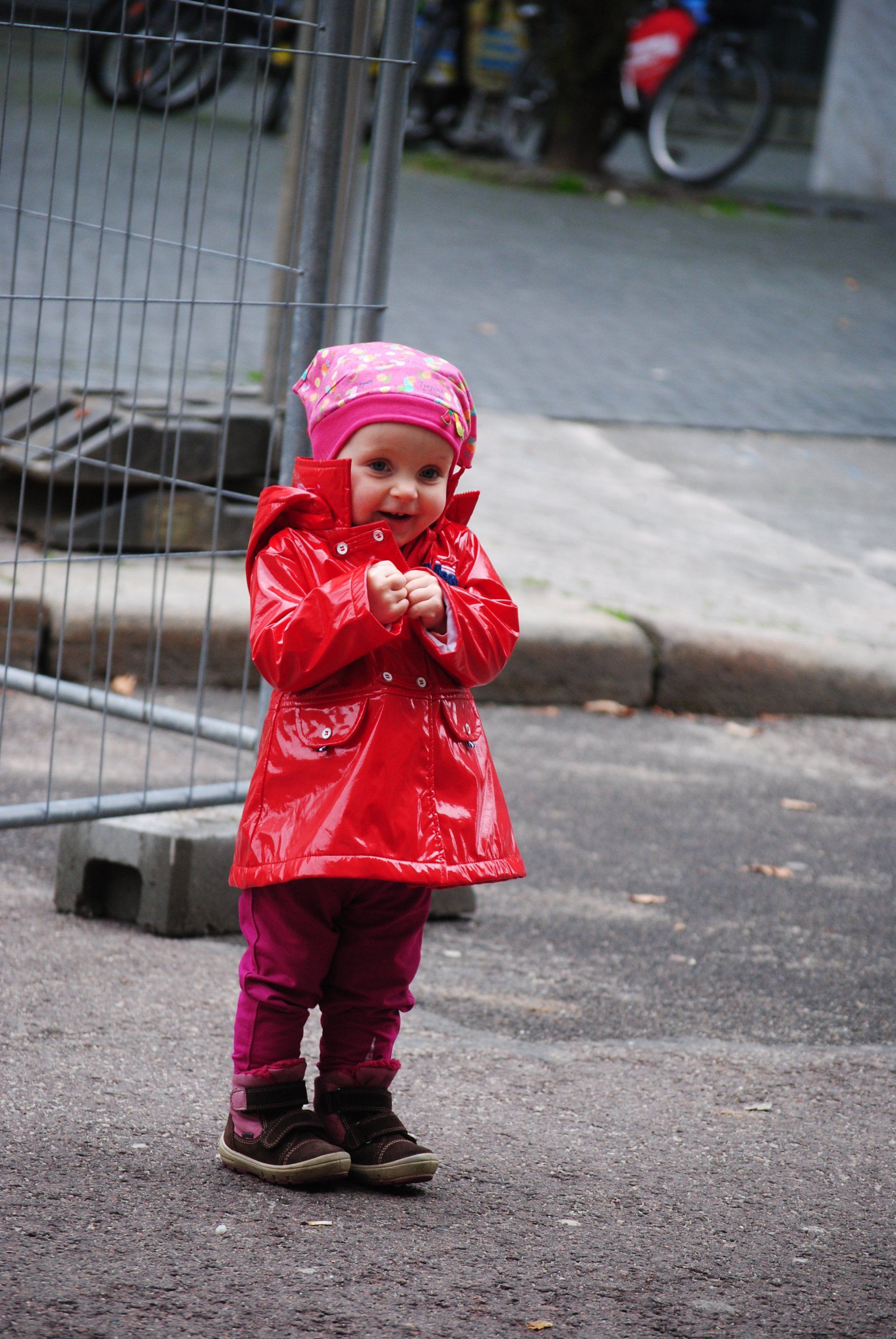 A little girl wearing a red raincoat and a pink hat