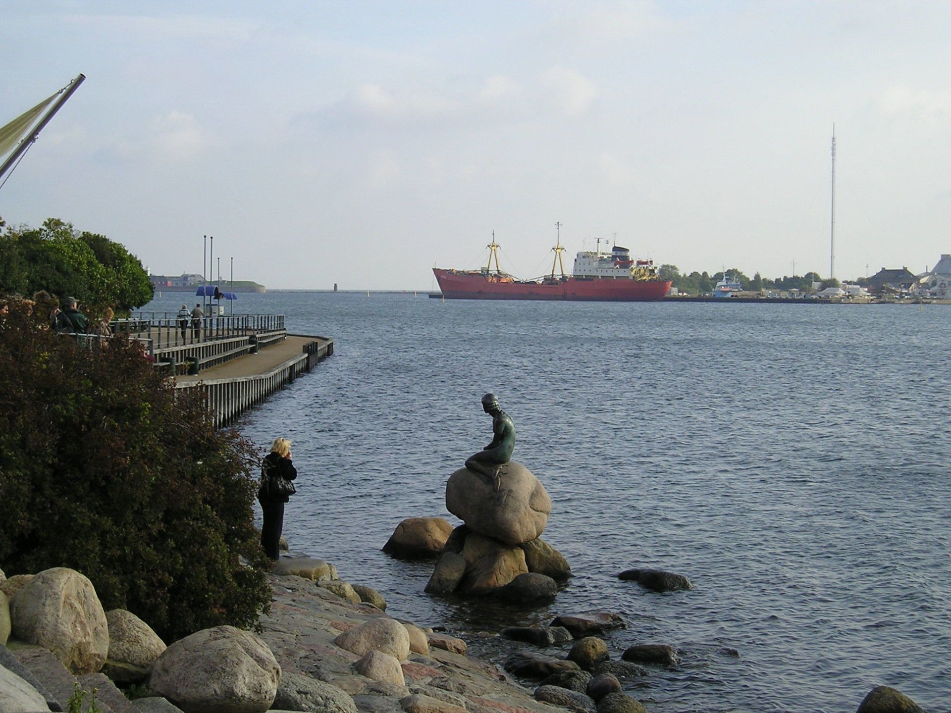 A statue of a mermaid sits on the shore of a body of water