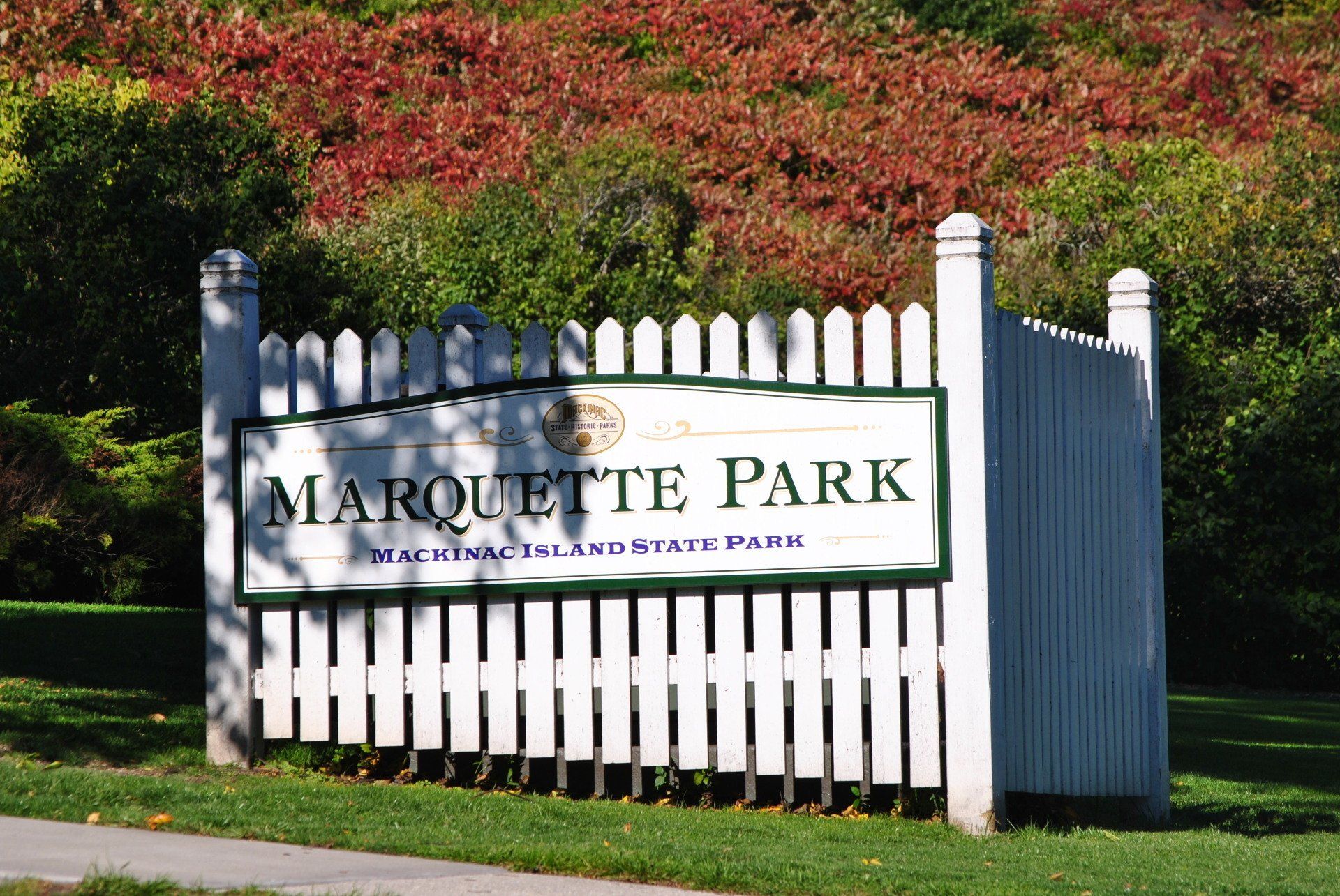 A sign for marquette park is behind a white picket fence