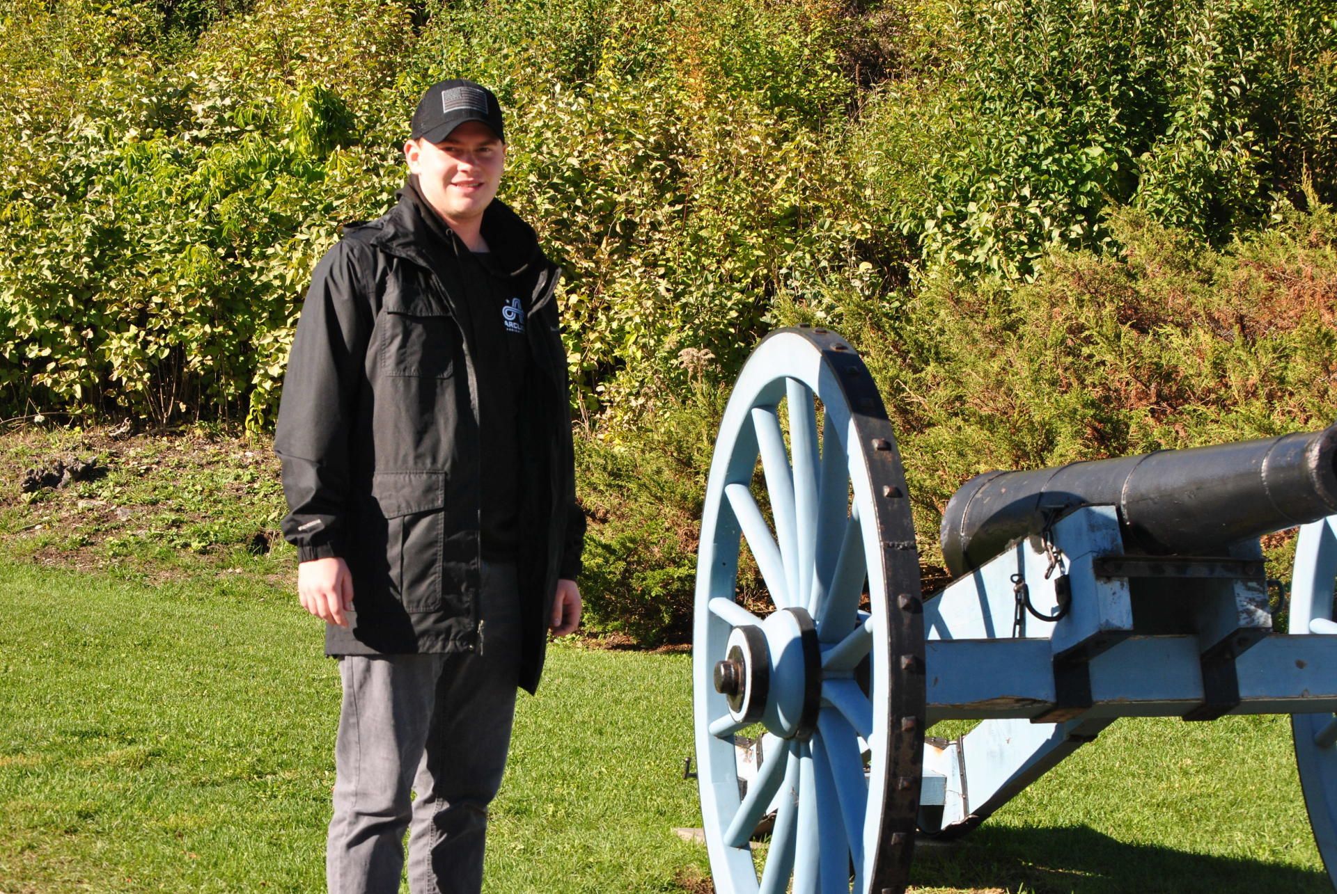 A man in a black jacket is standing next to a blue cannon.