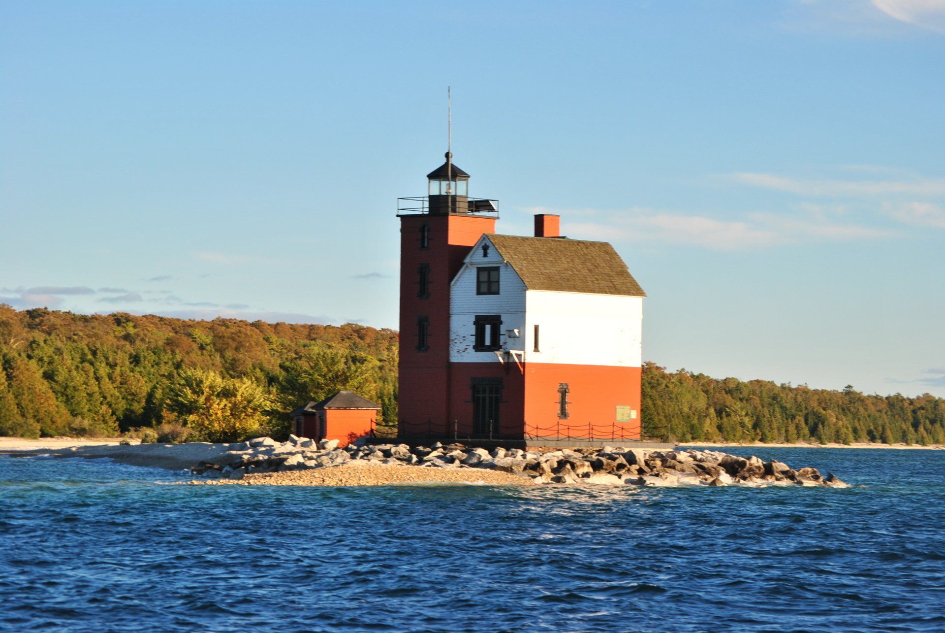 A red and white lighthouse sits on a small island in the middle of a body of water