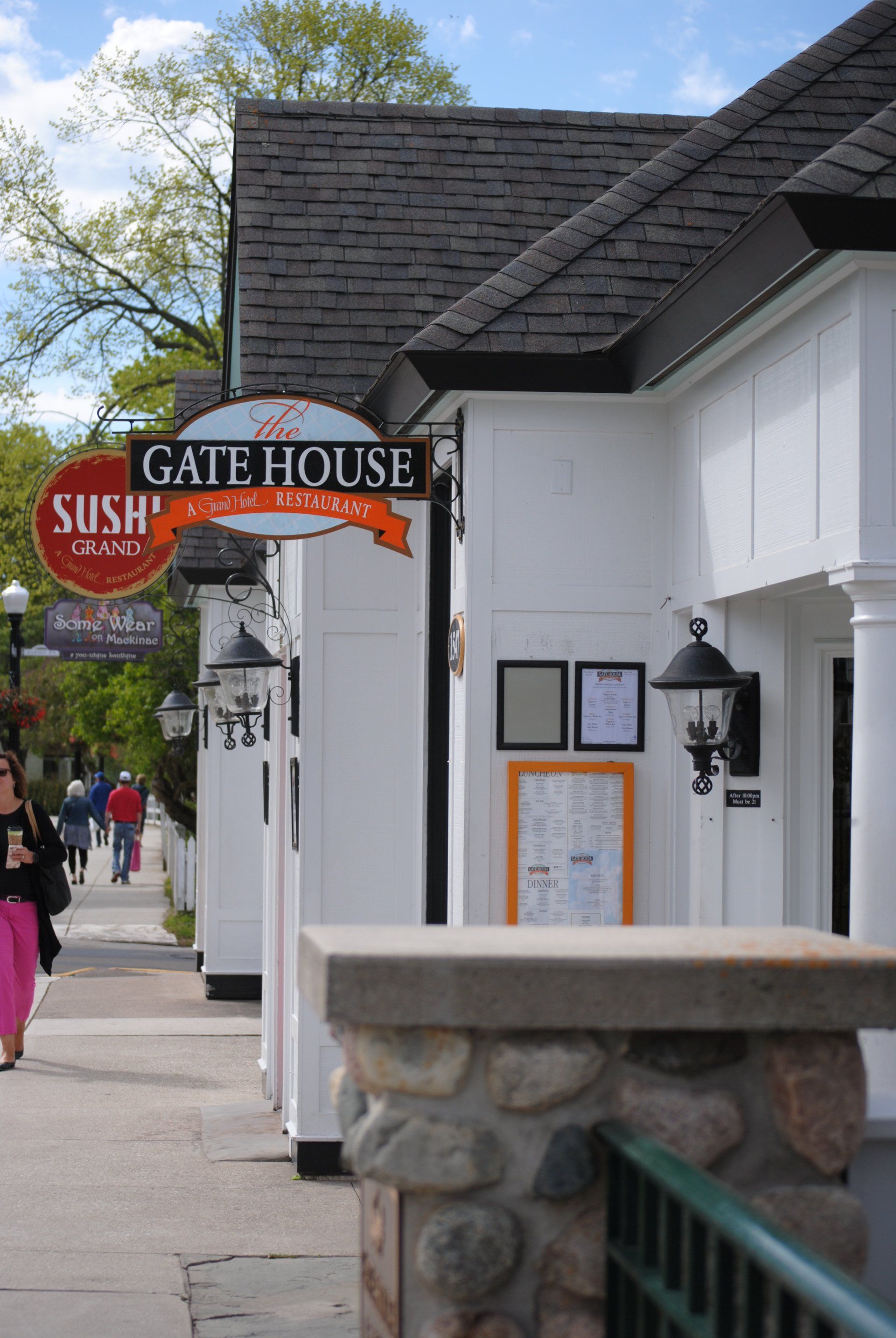 A woman walking down a sidewalk in front of a gate house restaurant