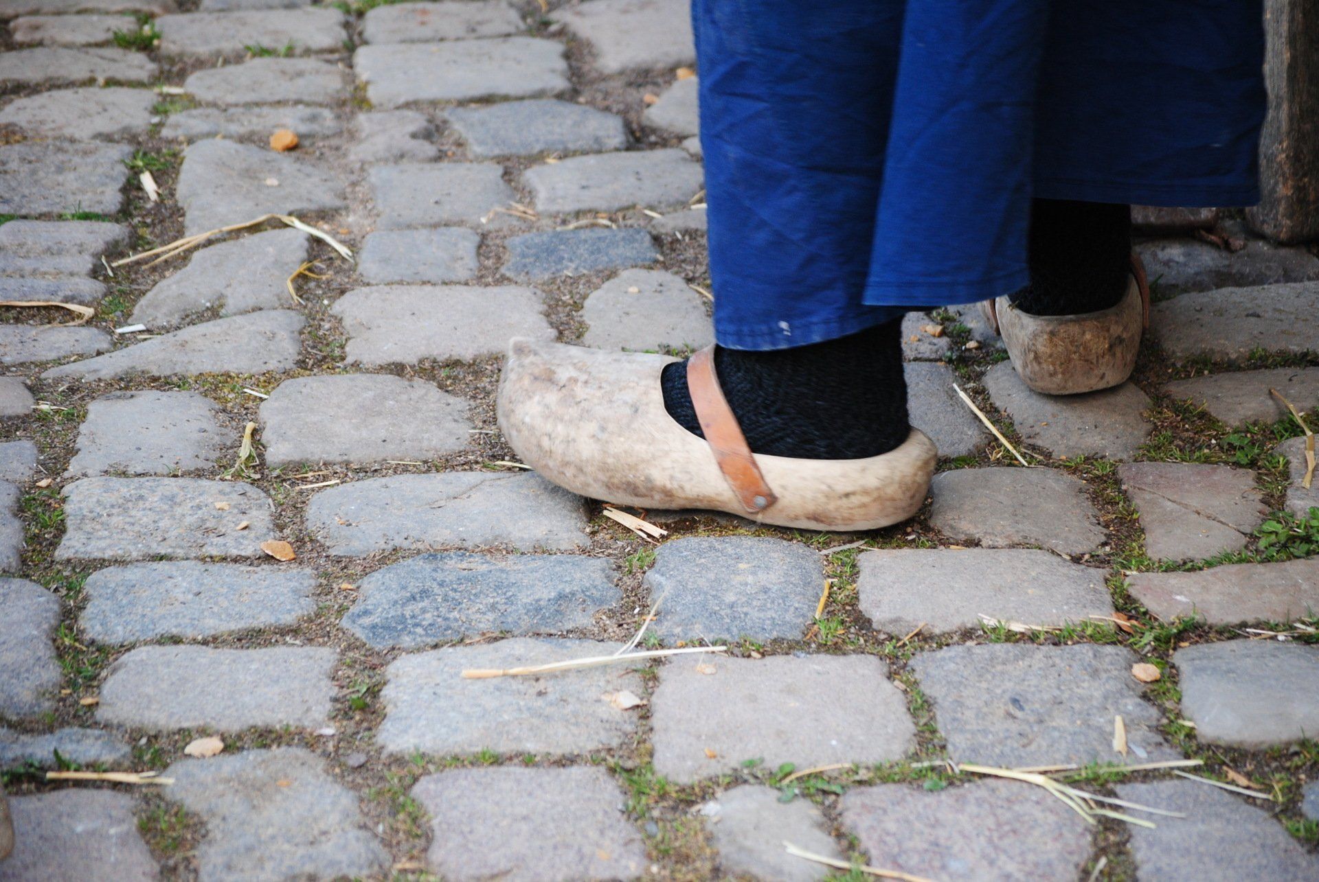 A person wearing a pair of wooden clogs on a cobblestone street.