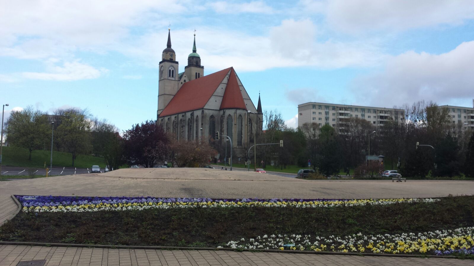 A large church with a red roof is surrounded by flowers in a park.