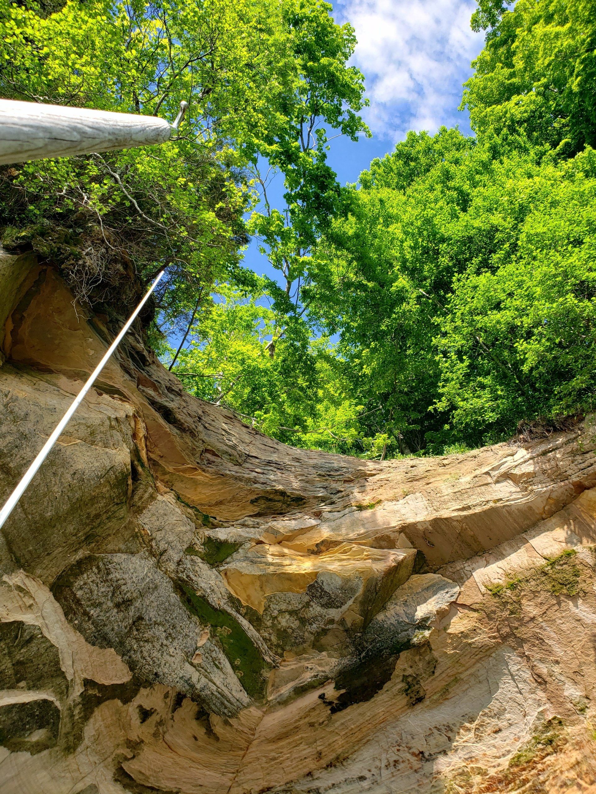 A person is standing on a rocky cliff with trees in the background.