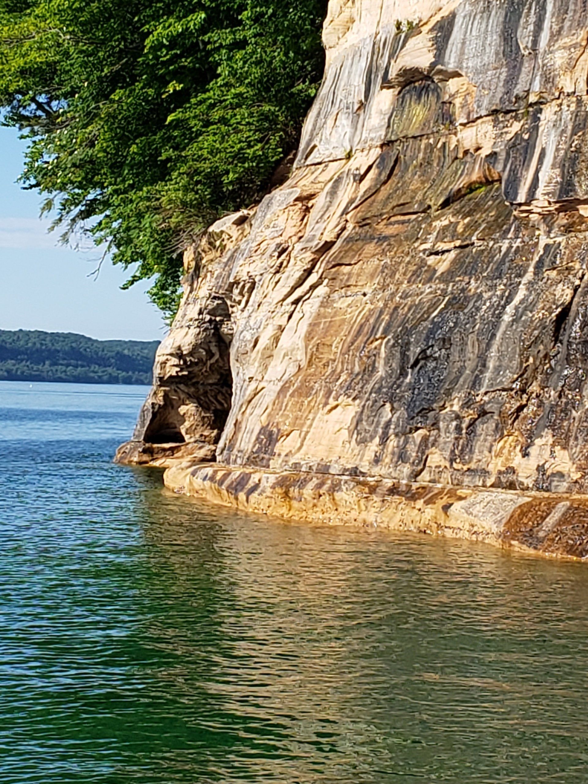 A large rocky cliff overlooking a lake with trees on the shore.