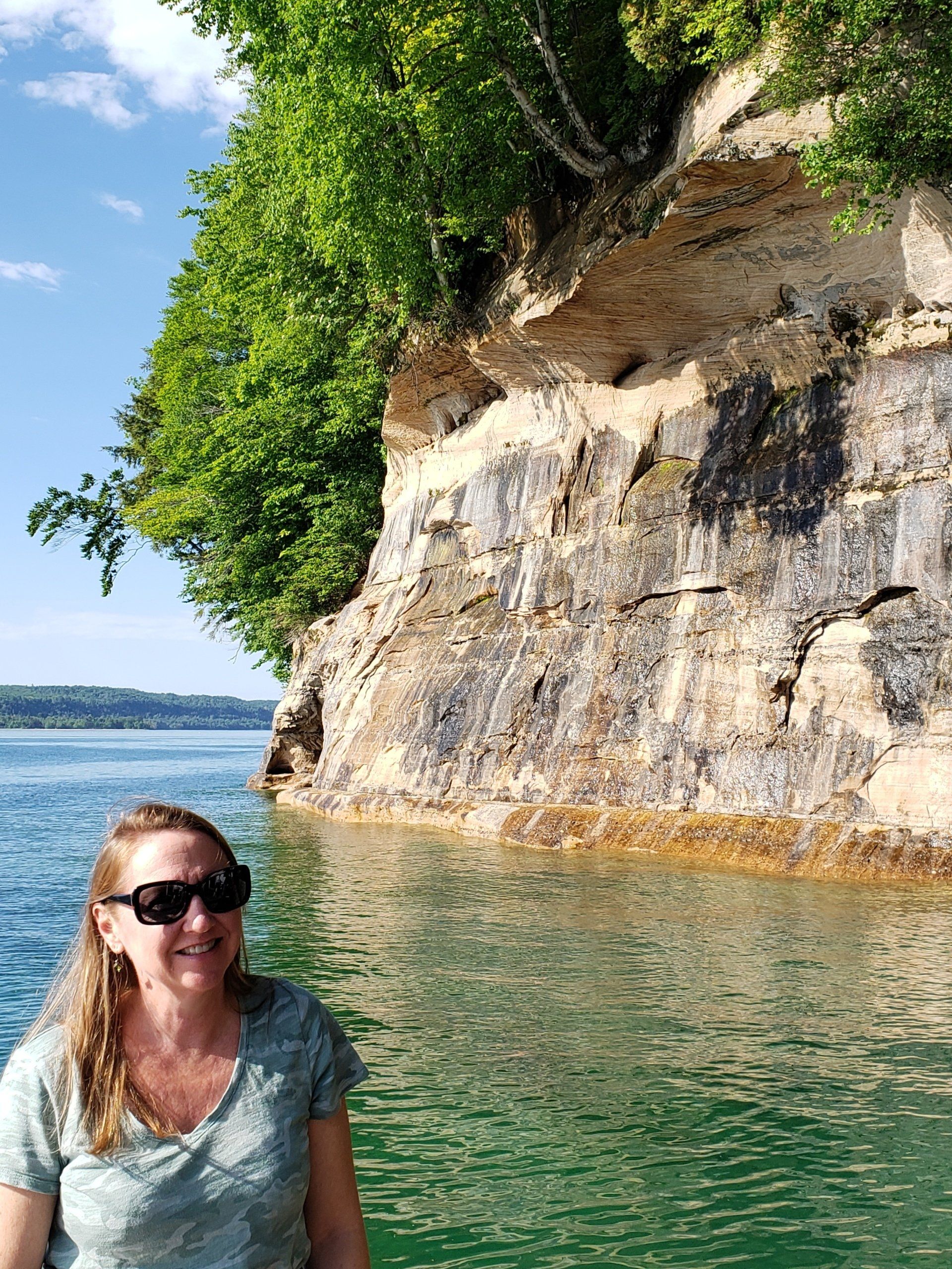 A woman is standing in the water near a rocky cliff.