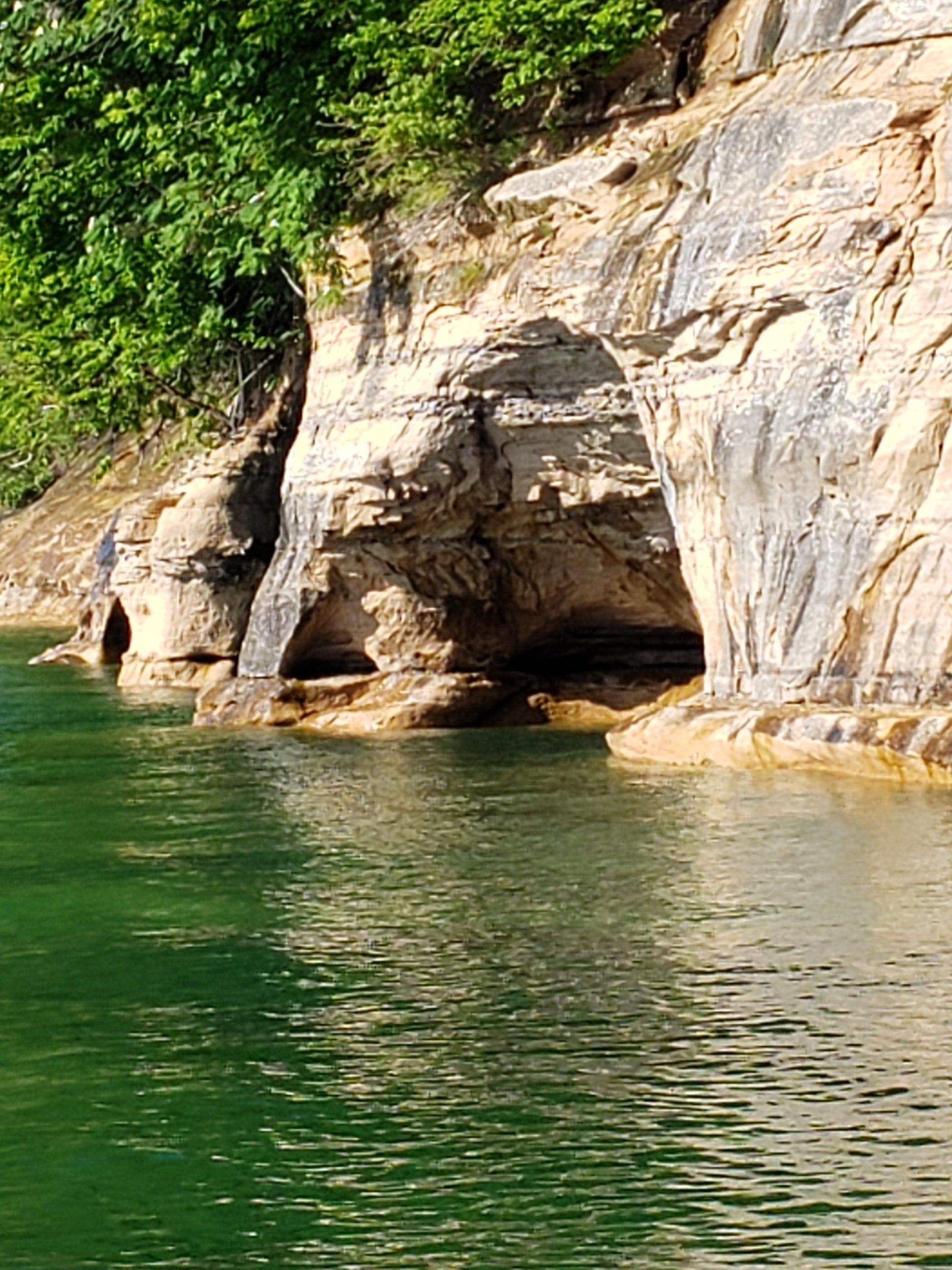 A cave in the middle of a lake next to a rocky cliff.