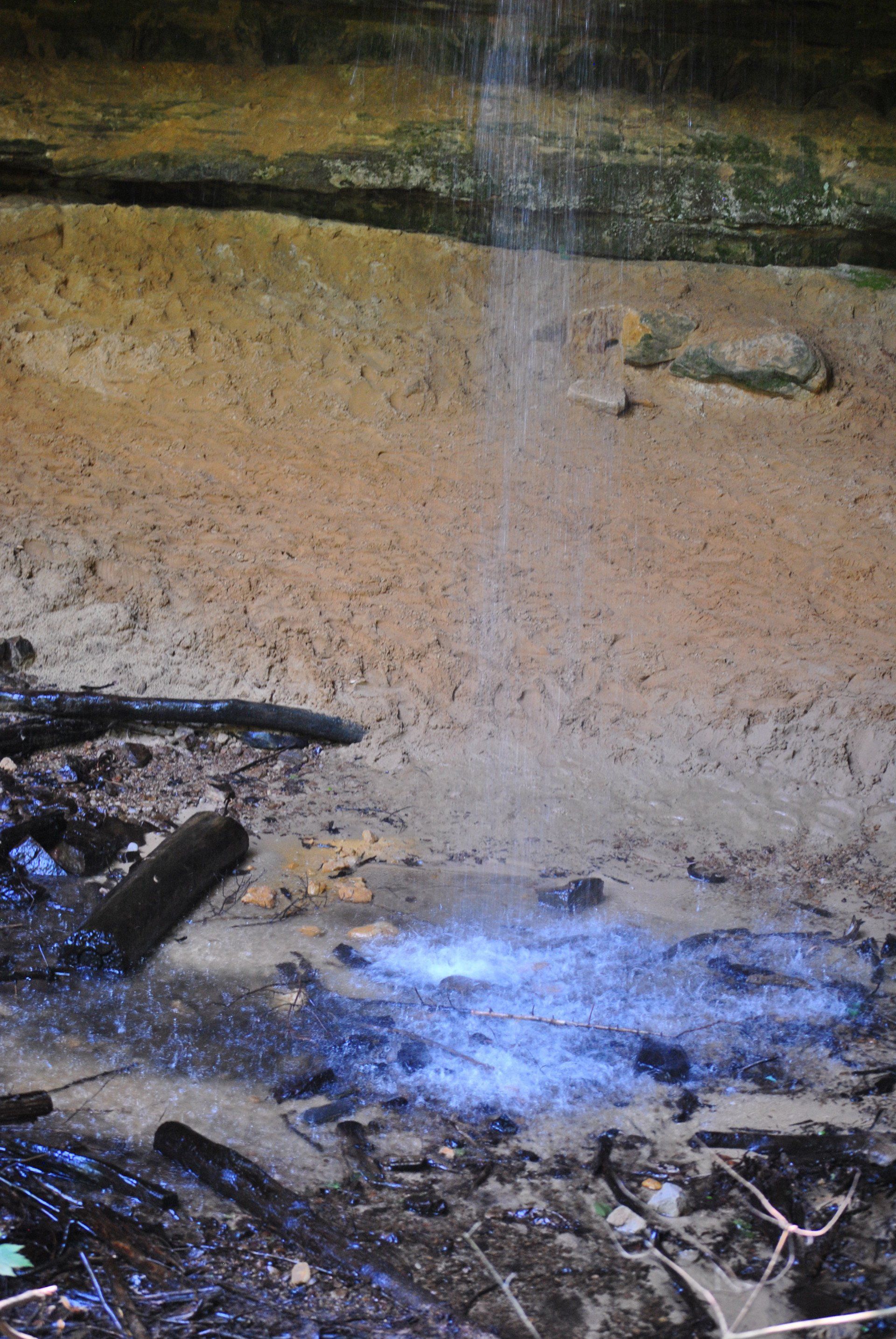 A close up of a waterfall in a cave with a blue light coming out of it.