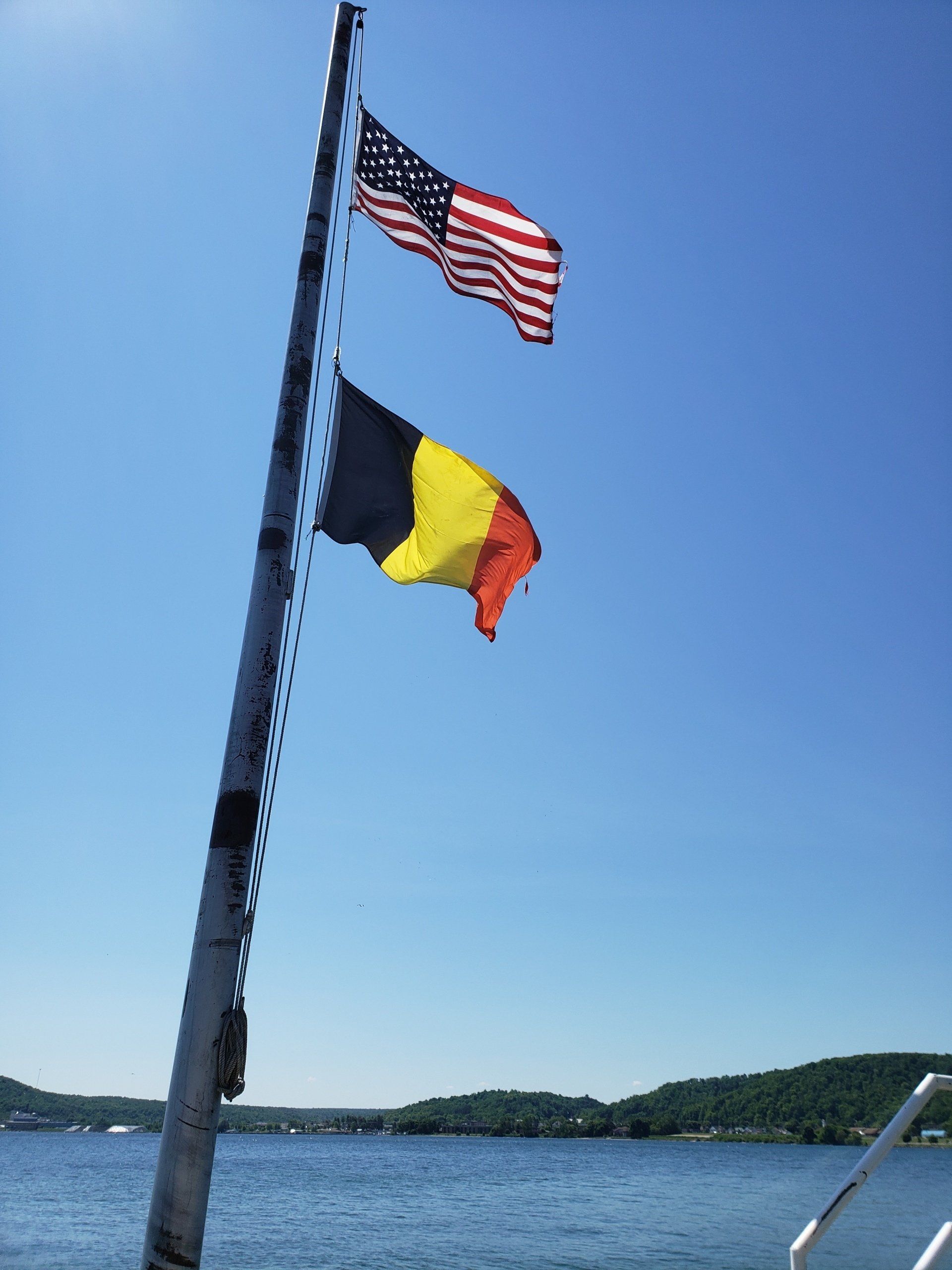 Two flags on a pole in front of a body of water