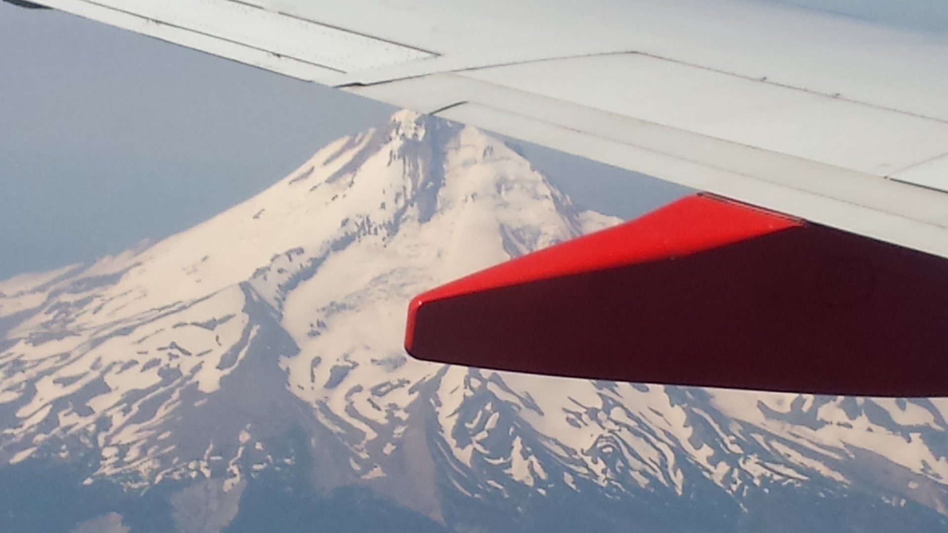 The wing of an airplane is shown with mountains in the background