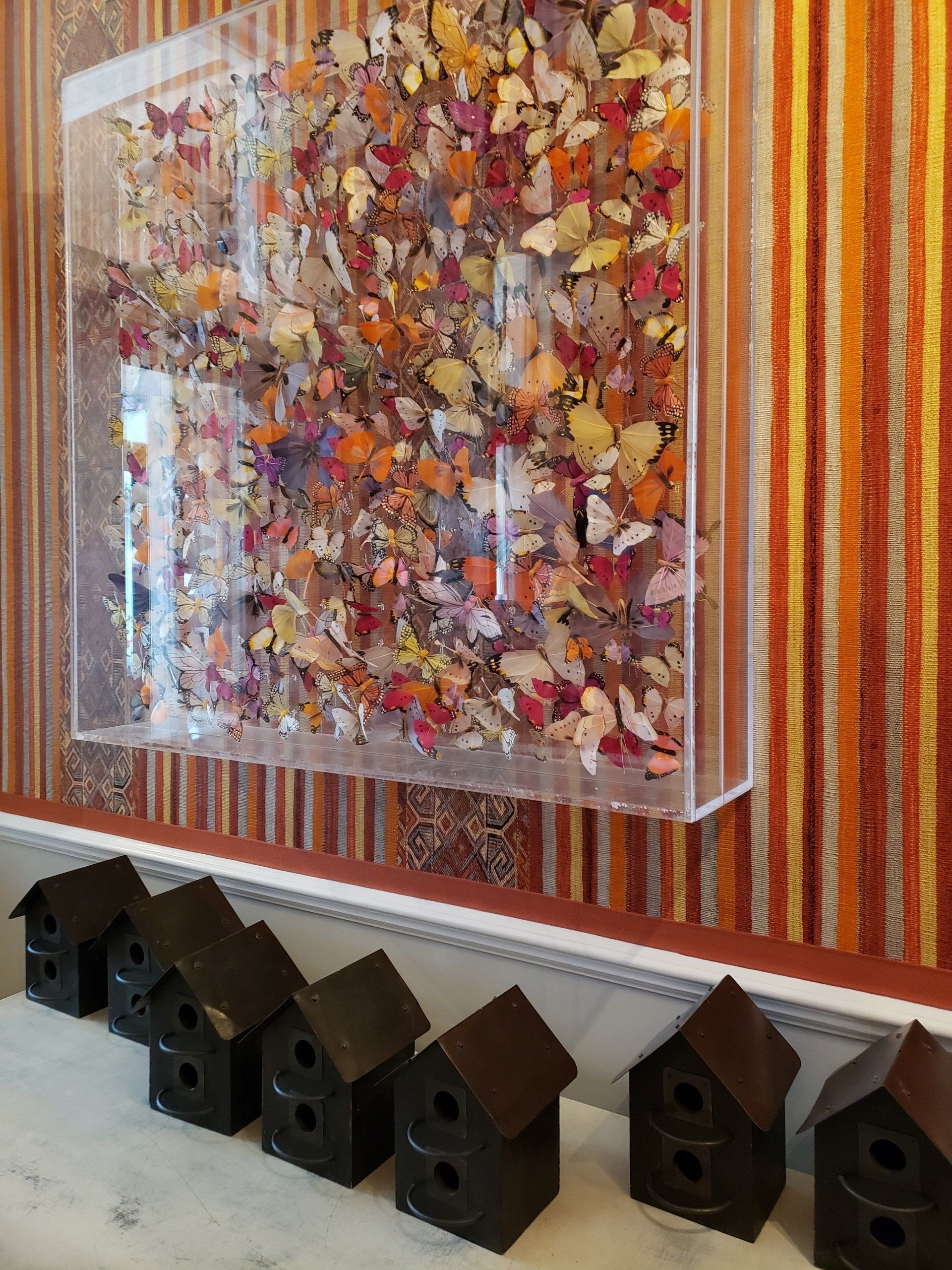 A row of small black houses are sitting on a table in front of a painting on a wall.