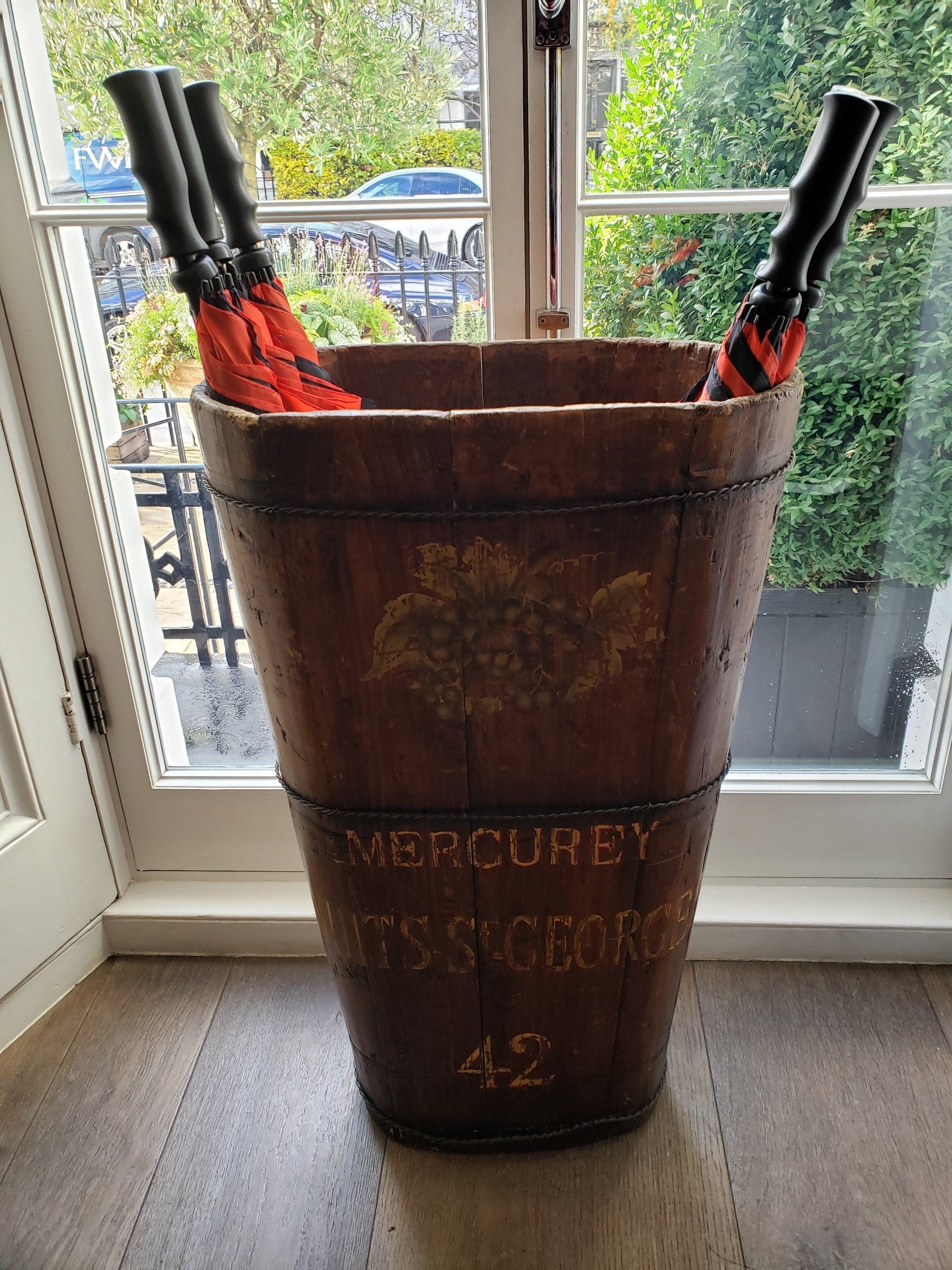 A wooden bucket filled with umbrellas is sitting in front of a window.